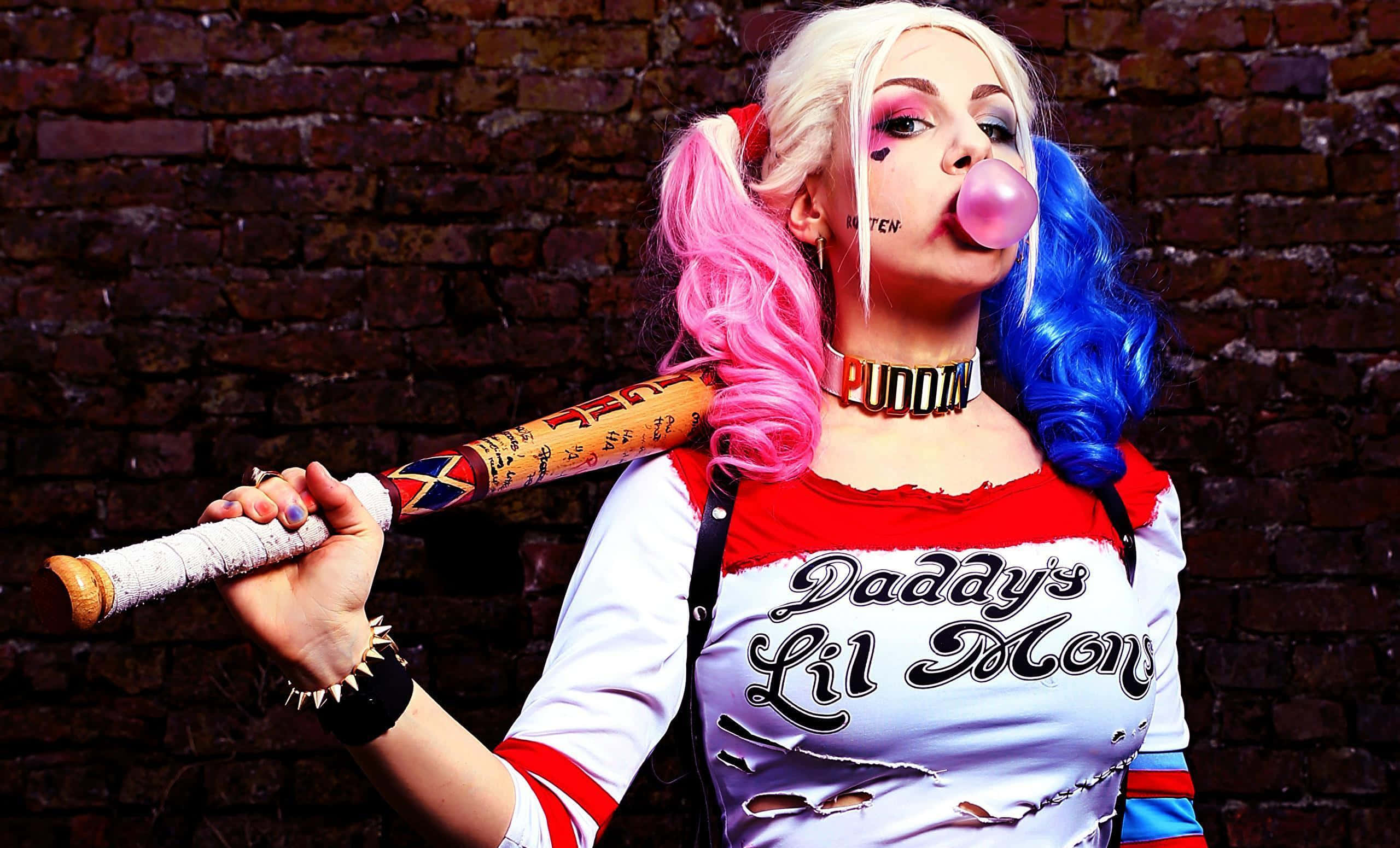Harley Quinn Baseball Bat 桌布 壁紙 — 一個扮演哈莉·奎茵嘅人，一邊對住磚牆揸住棒球棍，一邊吹住香口膠波。
