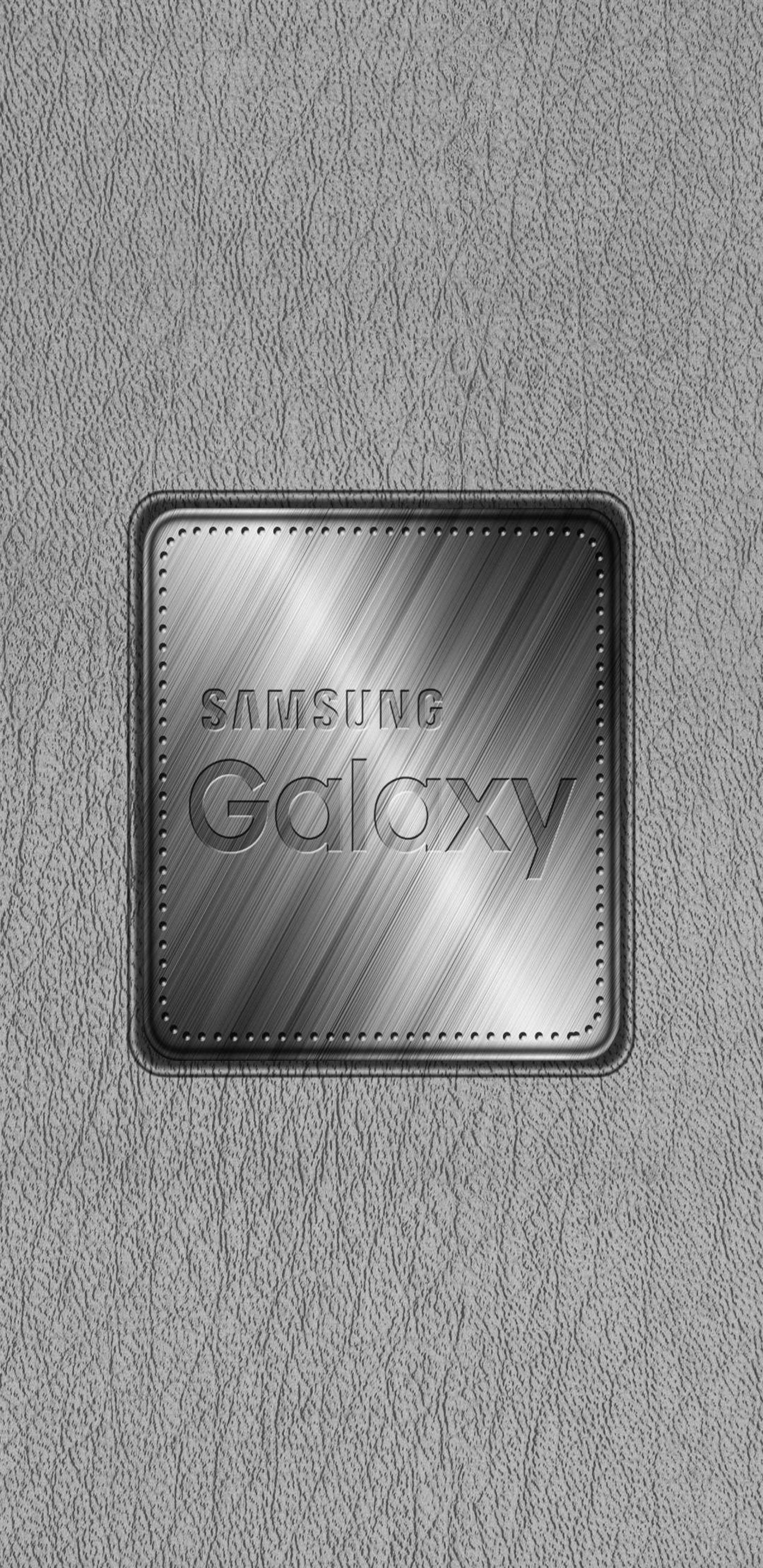 金屬動態圖 桌布 壁紙 — 一個拉絲金屬Samsung Galaxy標誌，居中於有紋理的灰色皮革背景上。