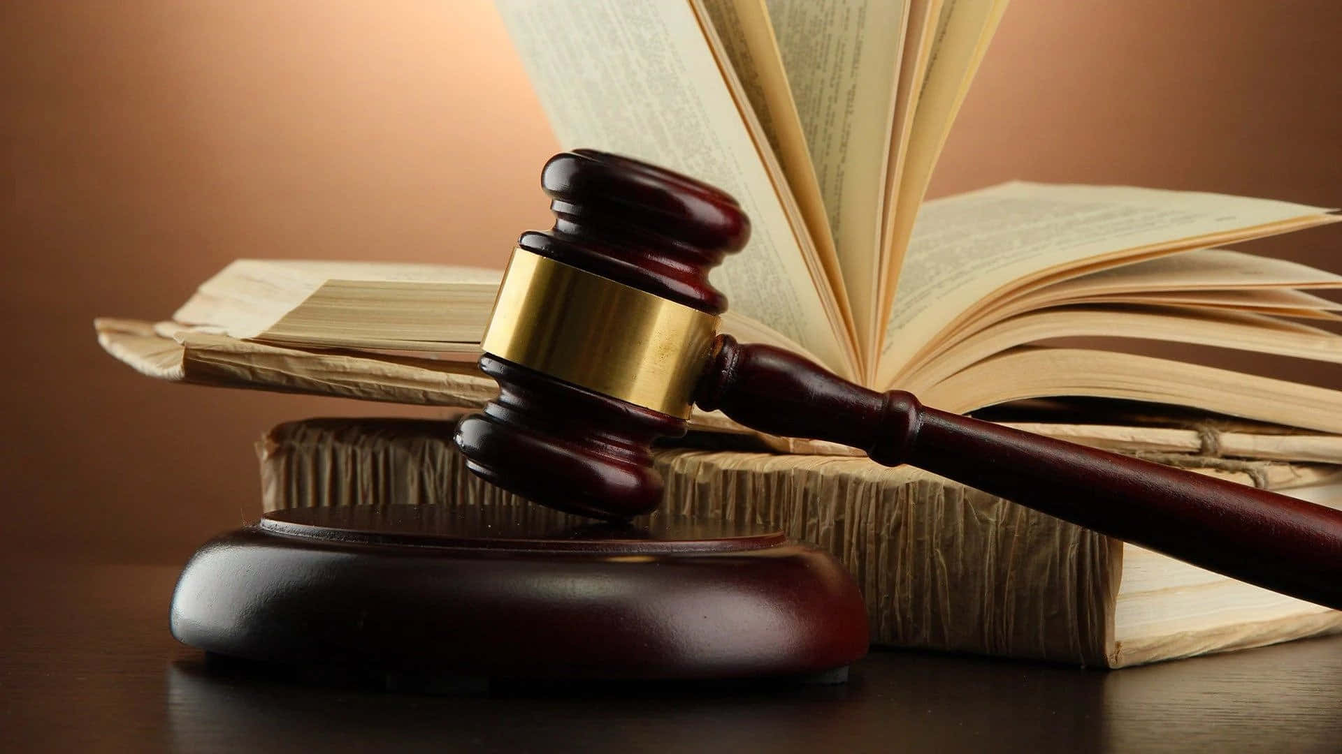 Law 桌布 壁紙 — 一個拋光木槌放在其支架上，置於一本打開的法律書前，伴隨溫暖的金色燈光。
