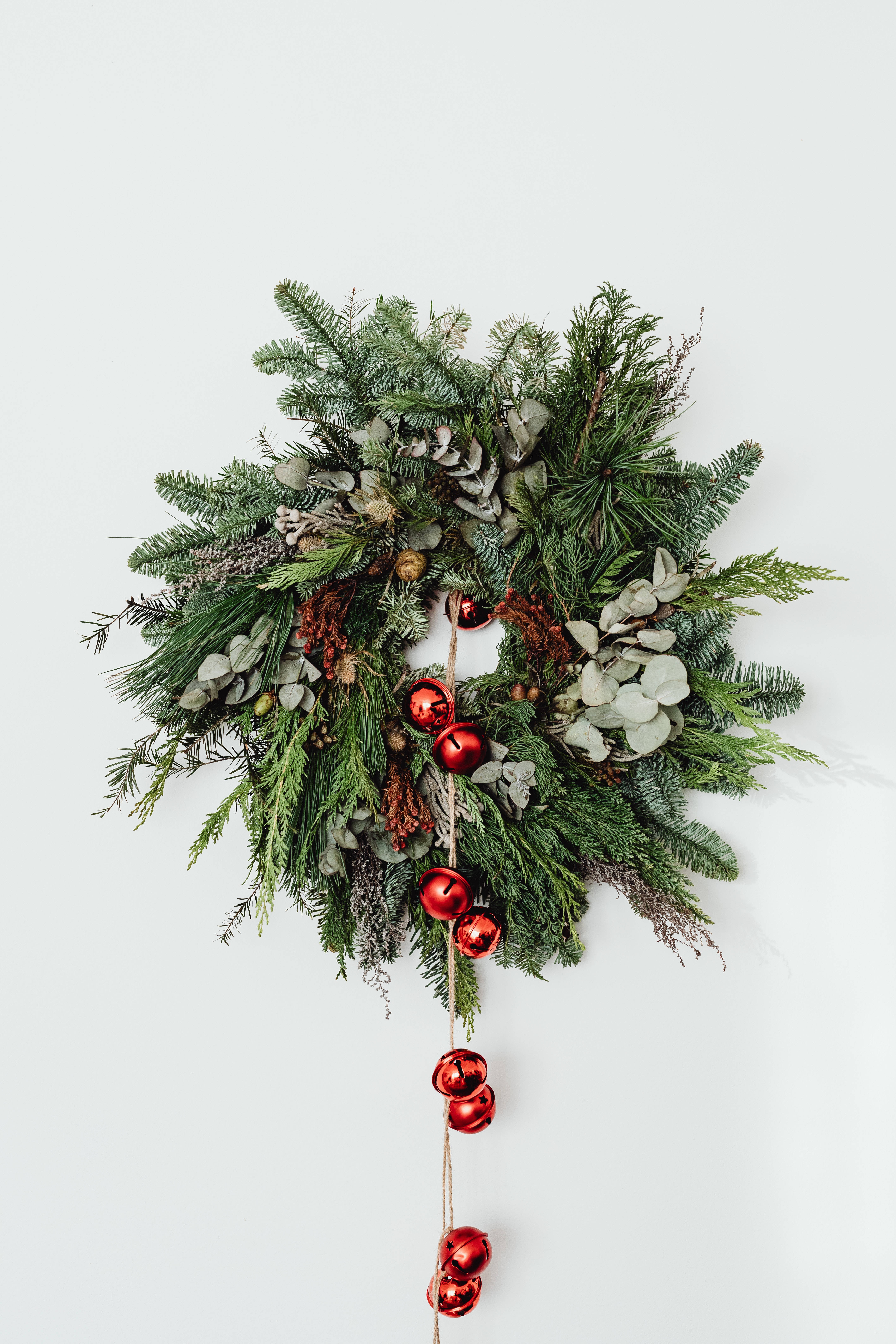Christmas Balls 桌布 壁紙 — 一個掛在純白牆上的翠綠聖誕花環，飾有紅色鈴鐺和松果。