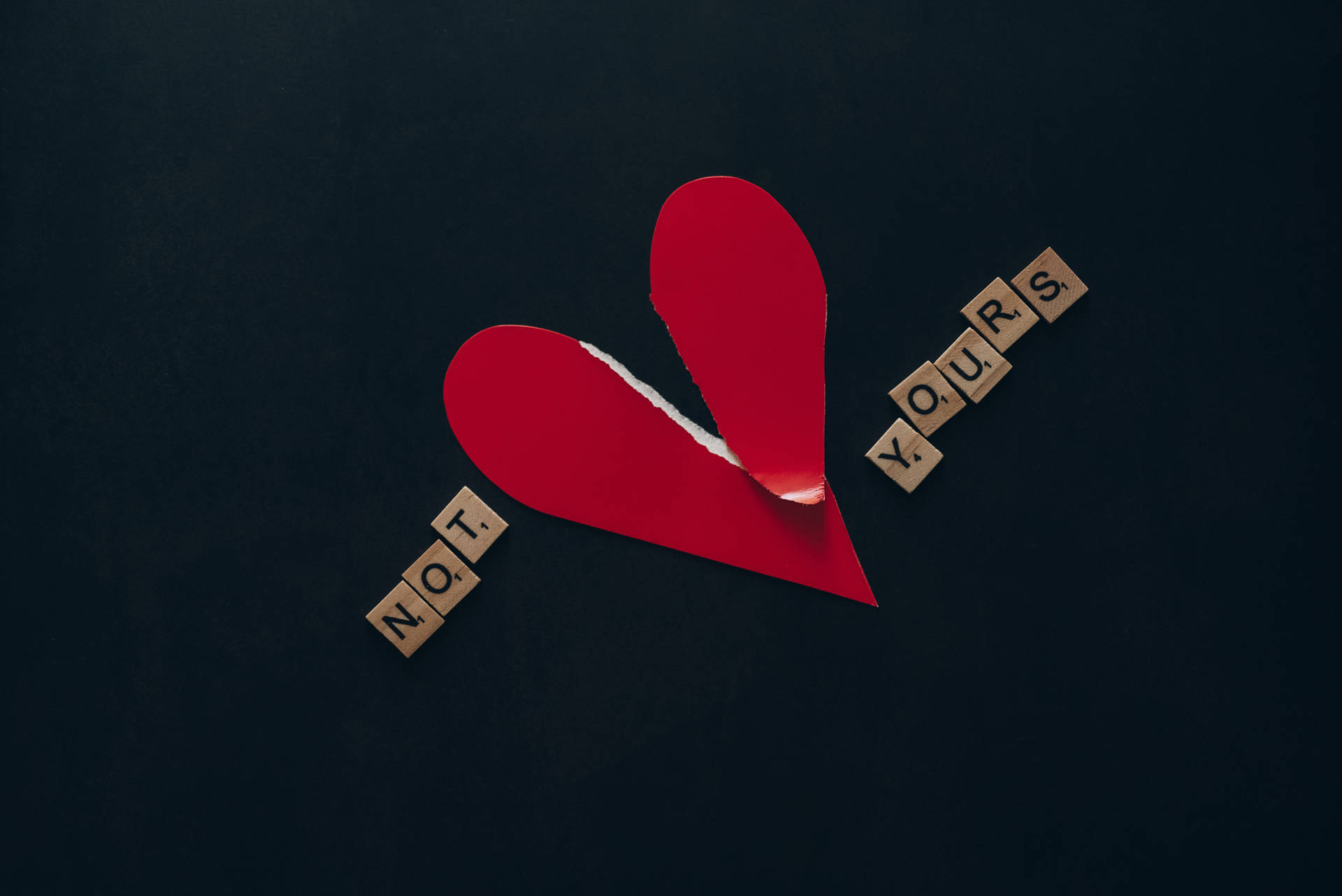 撕裂的紅色紙心心，帶有在深色背景上讀作「NOT YOURS」的木塊。 — 心碎 GIF 壁紙