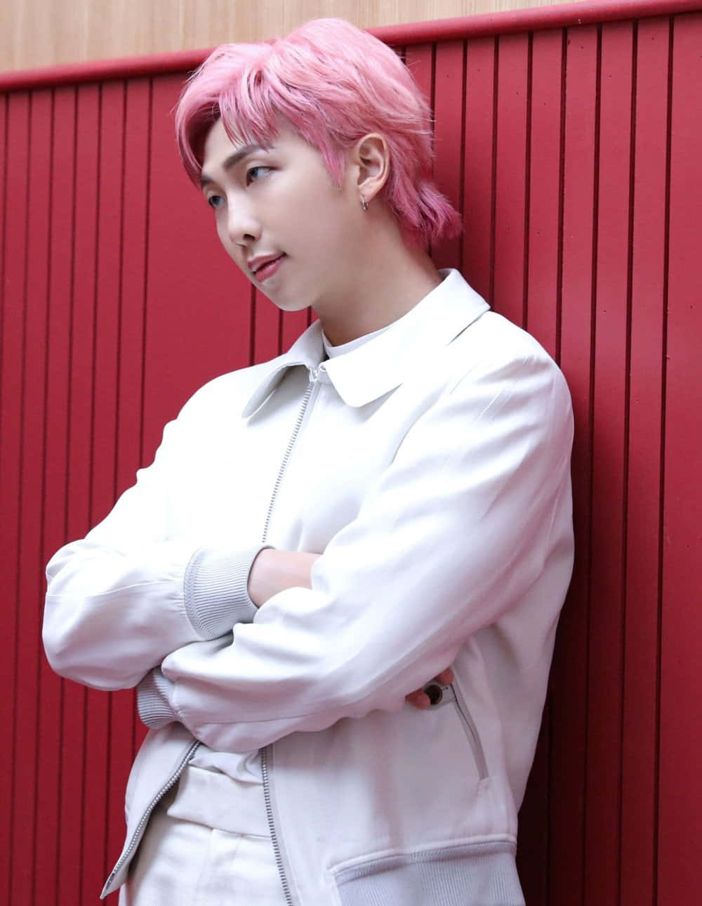 Namjoon 桌布 壁紙 — 一個擁有充滿活力的粉紅色頭髮的人靠著一面大膽的紅色木牆，穿著一件 crisp 白色外套，雙臂交叉。
