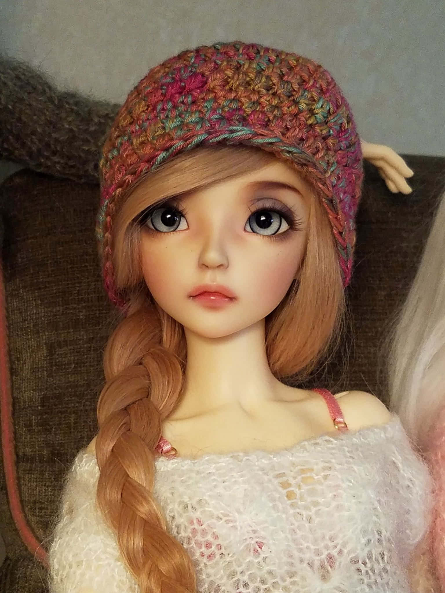 Dolls 桌布 壁紙 — 一個擁有大眼睛、表情豐富的公仔嘅特寫，戴住彩色鉤織帽同白色針織上衣。