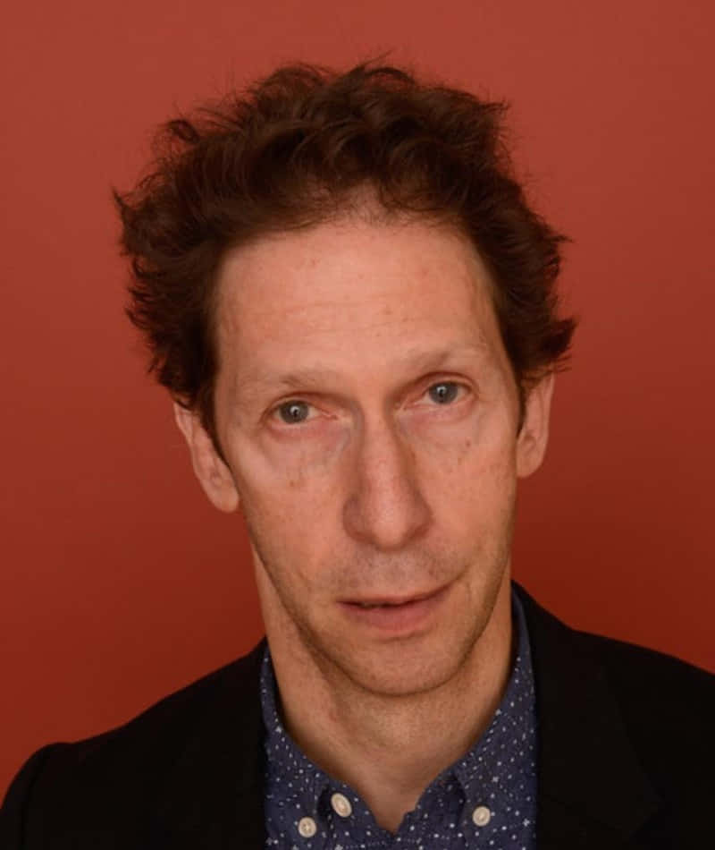 Tim Blake Nelson 桌布 壁紙 — 一個擁有棕色捲髮和藍眼睛的男人，在純紅色背景前直視鏡頭。
