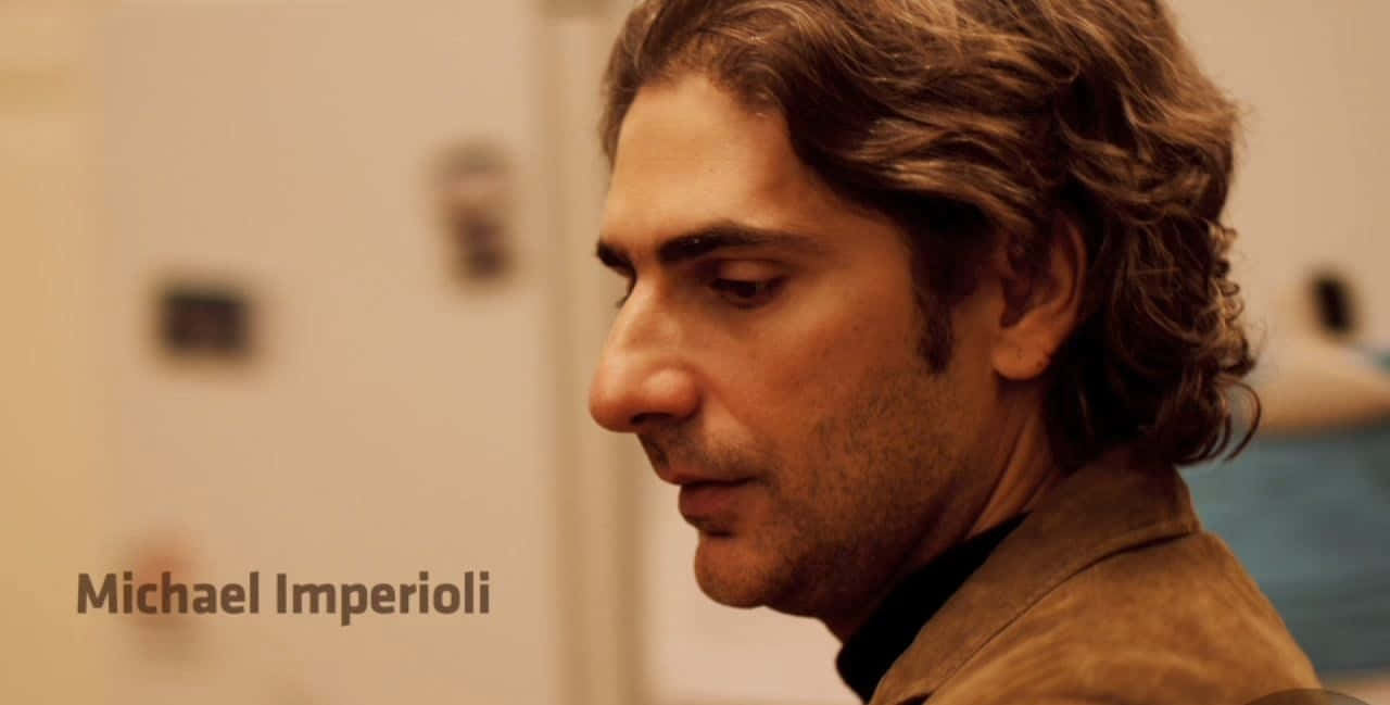 Michael Imperioli 桌布 壁紙 — 一個擁有波浪形棕色頭髮的男人在溫暖照明的室內環境中向下看的特寫側面。