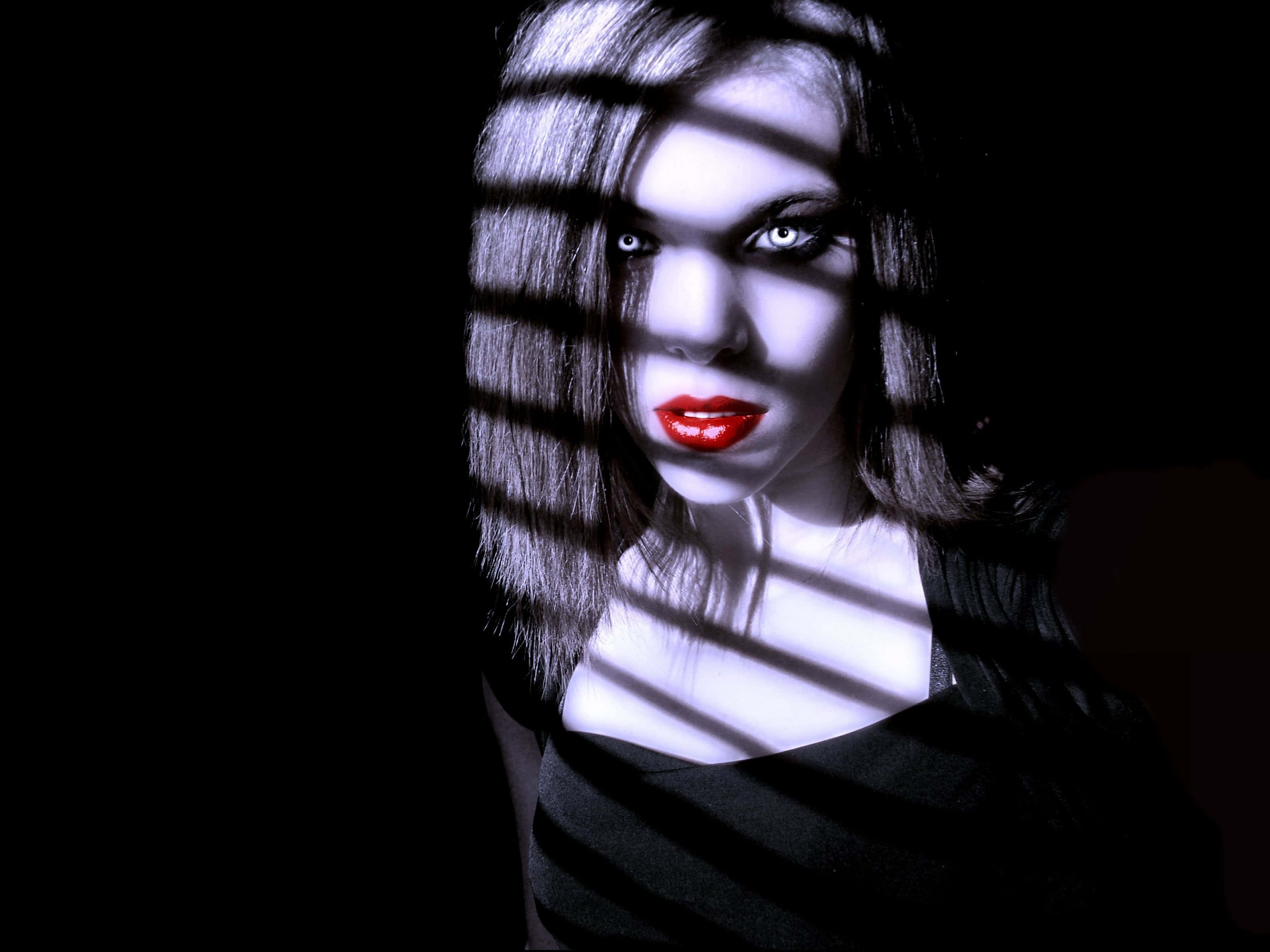 Dark Vampire 桌布 壁紙 — 一個擁有發光眼睛和紅唇的女人，在黑暗的房間裡透過百葉窗凝視，百葉窗在她臉上投下鮮明的陰影。