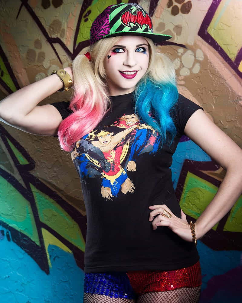 Harley Quinn Cosplay 桌布 壁紙 — 一個擁有色彩繽紛頭髮和大膽妝容的人，自信地在一幅充滿活力的塗鴉牆前擺姿勢，穿著漫畫T恤和閃亮短褲。