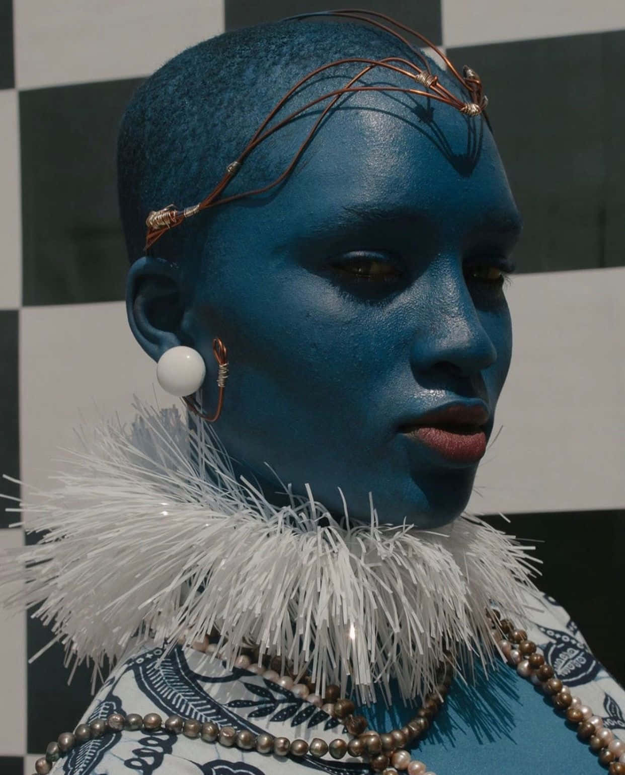 Afrofuturism 桌布 壁紙 — 一個擁有藍色皮膚和銅線頭飾的人，在黑白格仔背景前擺姿勢。