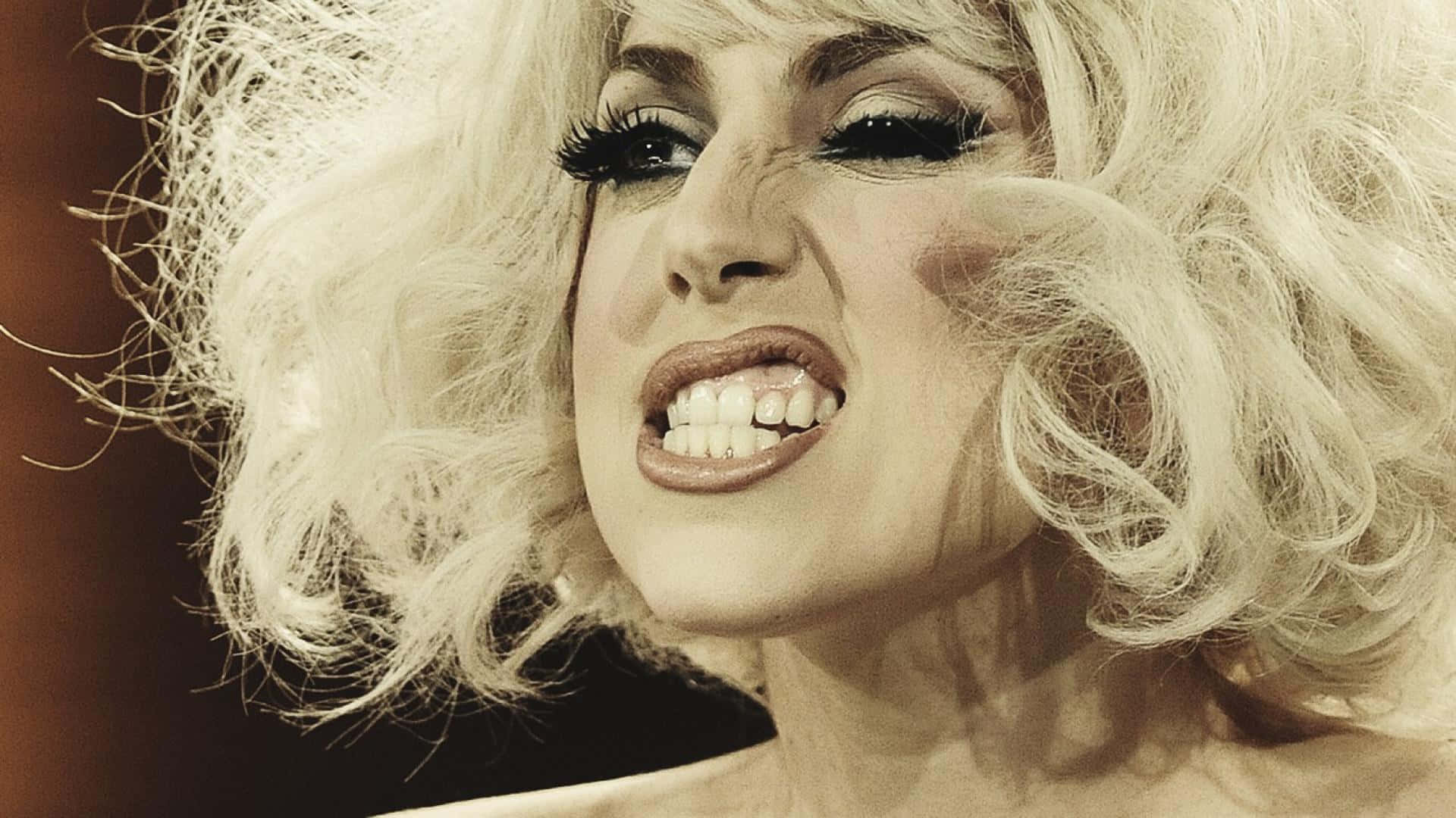 Lady Gaga 桌布 壁紙 — 一個擁有豐盈金髮和戲劇化妝容的人，帶著強烈表情尖叫的特寫。