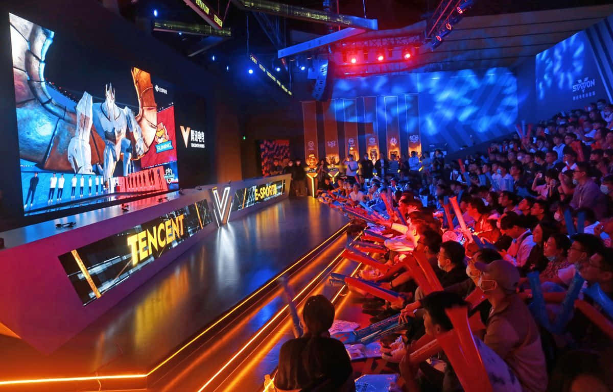 Esports 桌布 壁紙 — 一個擠滿人的電競場館，紅藍燈光閃爍，粉絲們正在巨型屏幕上觀看充滿活力的動畫遊戲。