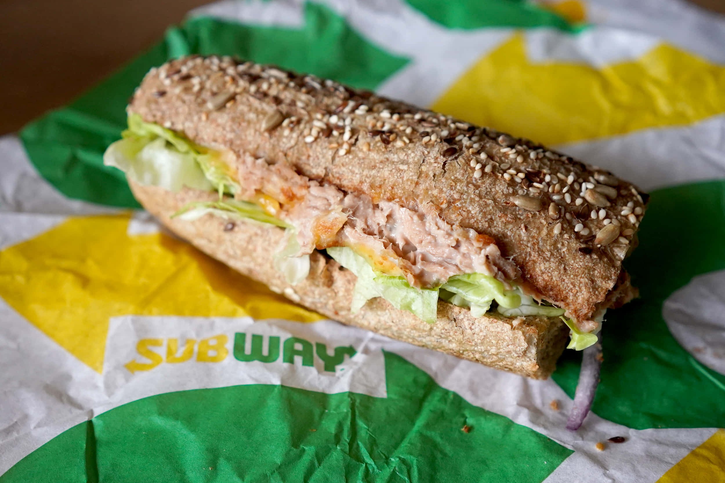 Subway 桌布 壁紙 — 一個新鮮製作的Subway三文治，配芝麻麵包和吞拿魚沙律，放在品牌紙上。