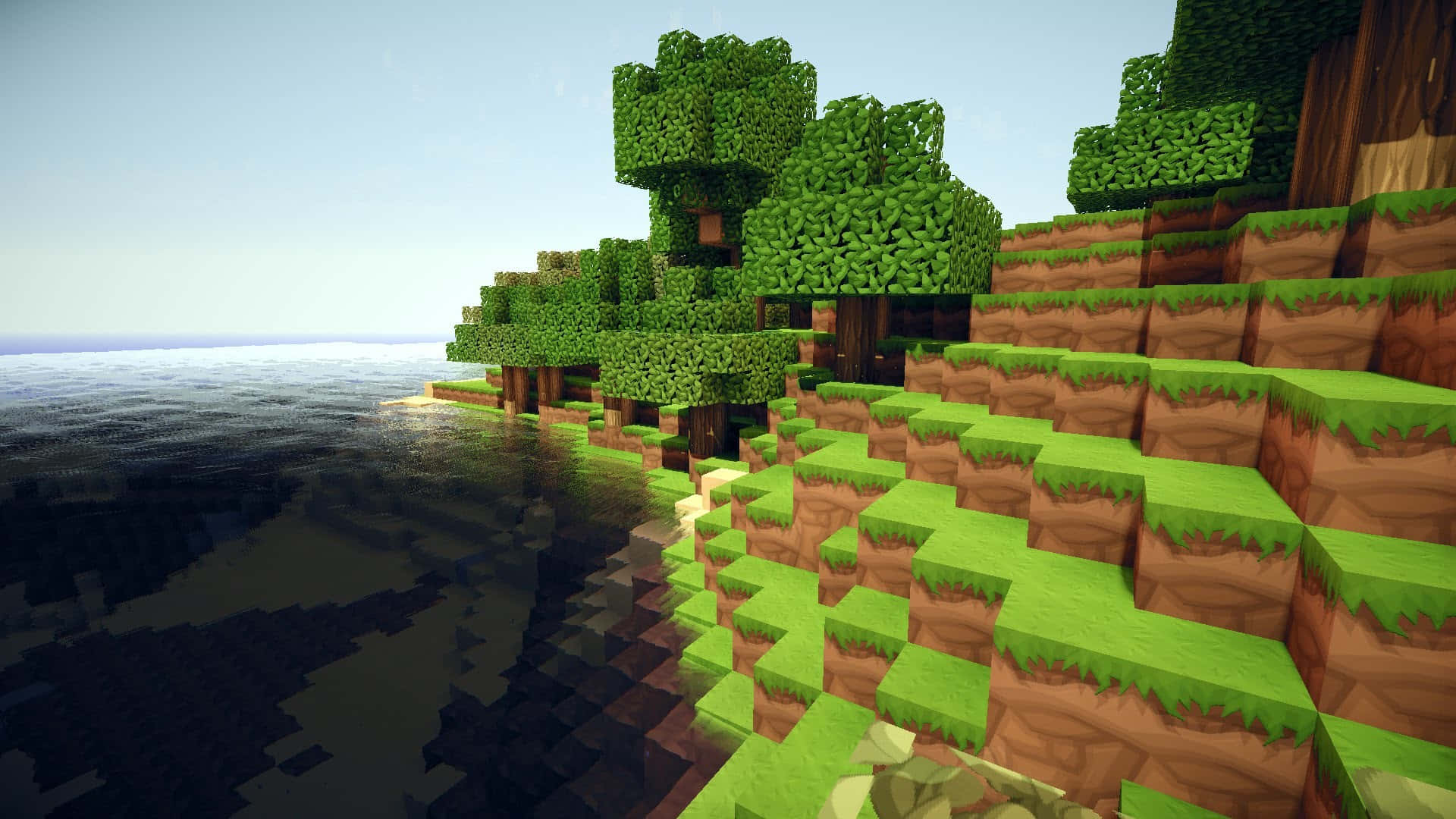 型格 Minecraft 桌布 壁紙 — 一個方塊狀的Minecraft海岸線，像素化的樹木和長滿草的懸崖在晴朗的天空下與平靜的海水相遇。