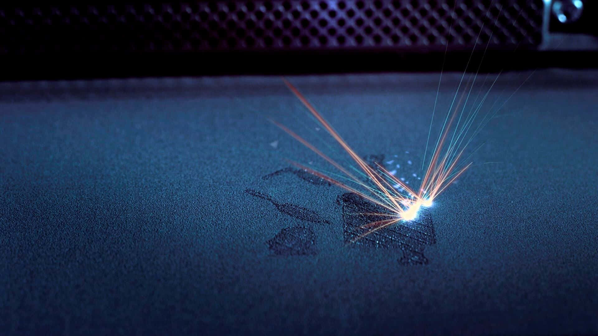 3d Printer 桌布 壁紙 — 一個明亮的激光點在昏暗燈光下，於深色紋理表面激起鮮豔的橙色和藍色軌跡。