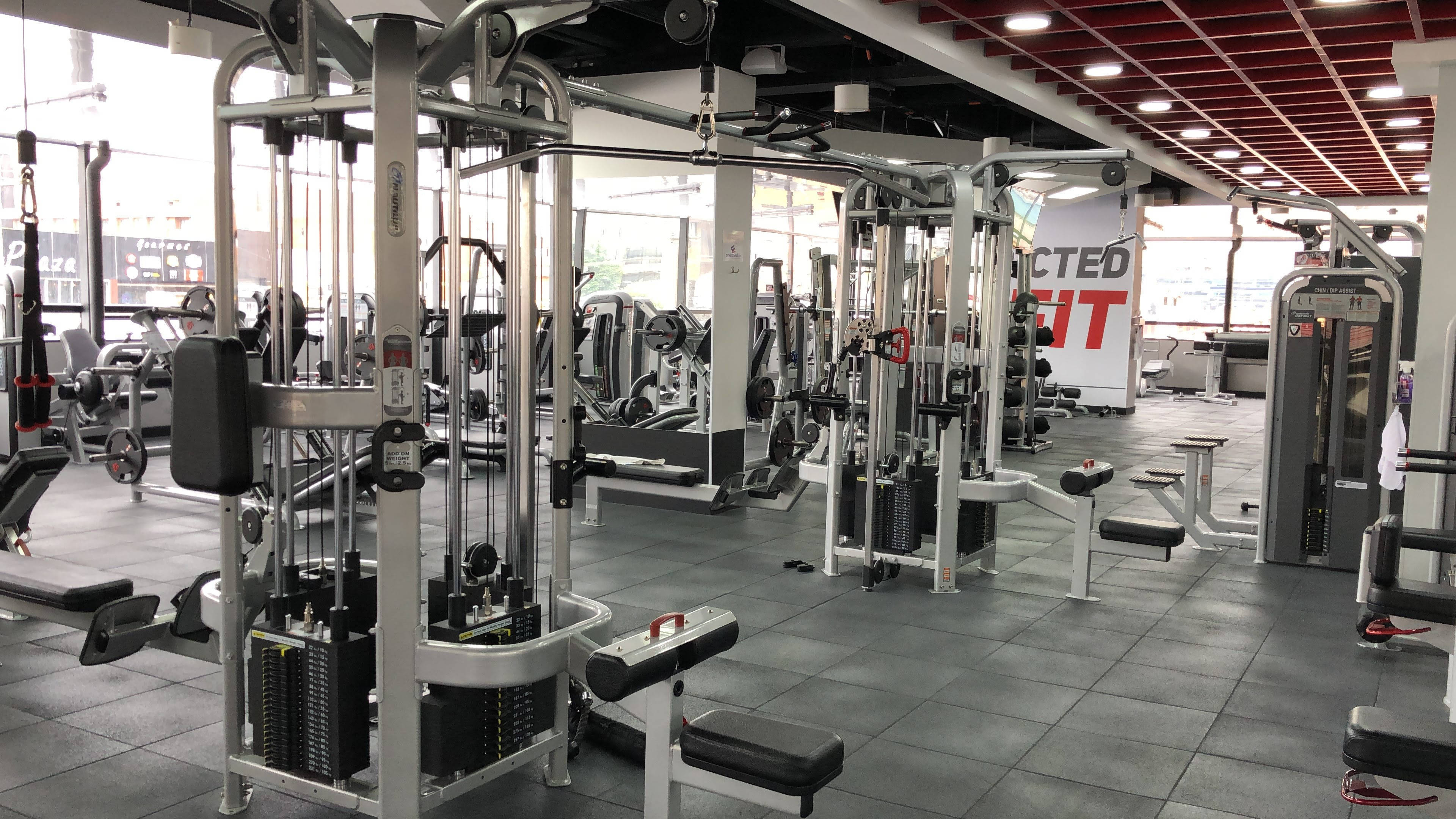 Exercise 桌布 壁紙 — 一個明亮的現代健身房，在紅色天花板面板下排列著一排排的重量訓練機和有氧運動設備。