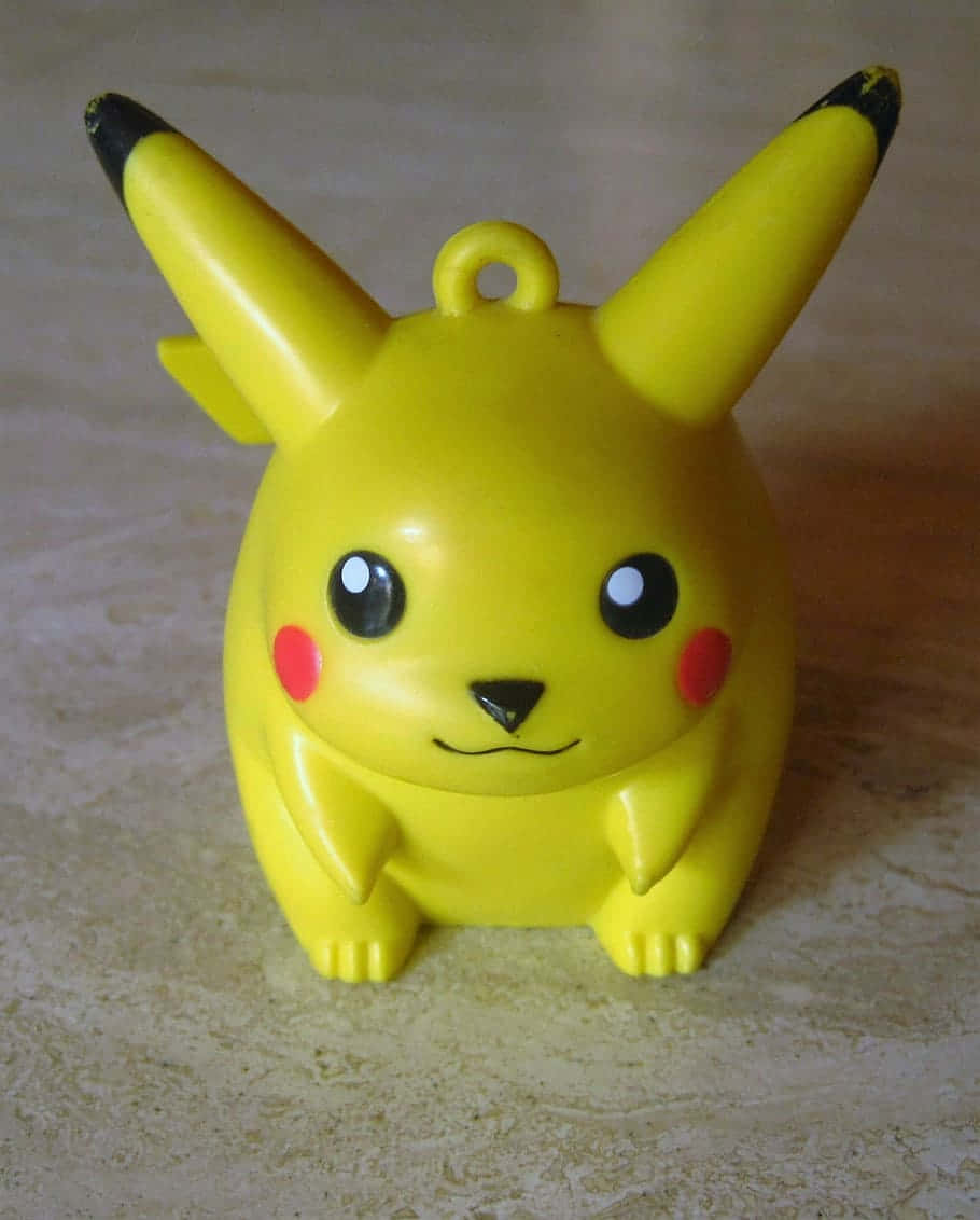 Pokemon Toys 桌布 壁紙 — 一個明亮的黃色比卡超公仔，有紅色臉頰和黑色尖端耳朵，坐在米色瓷磚表面上。