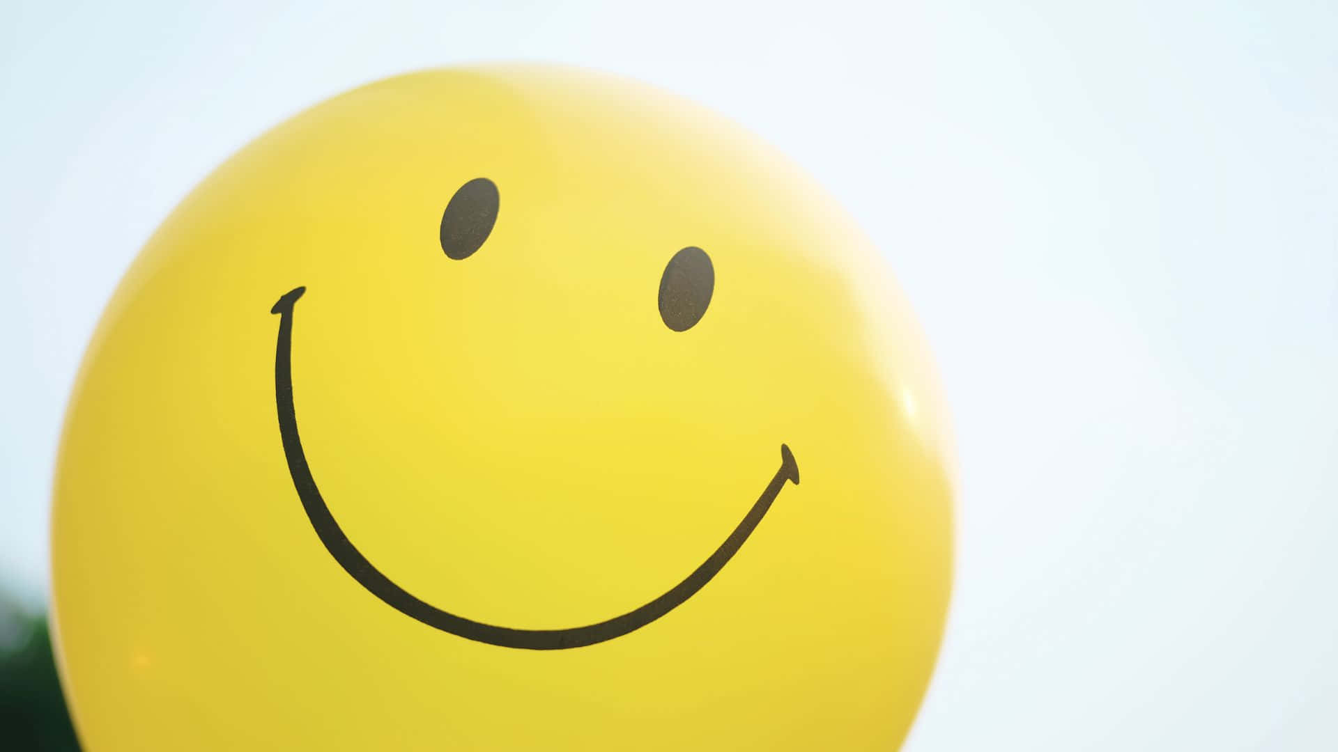 Smiley 桌布 壁紙 — 一個明亮的黃色氣球，帶有簡單的黑色笑臉設計，背景是柔和的白色。