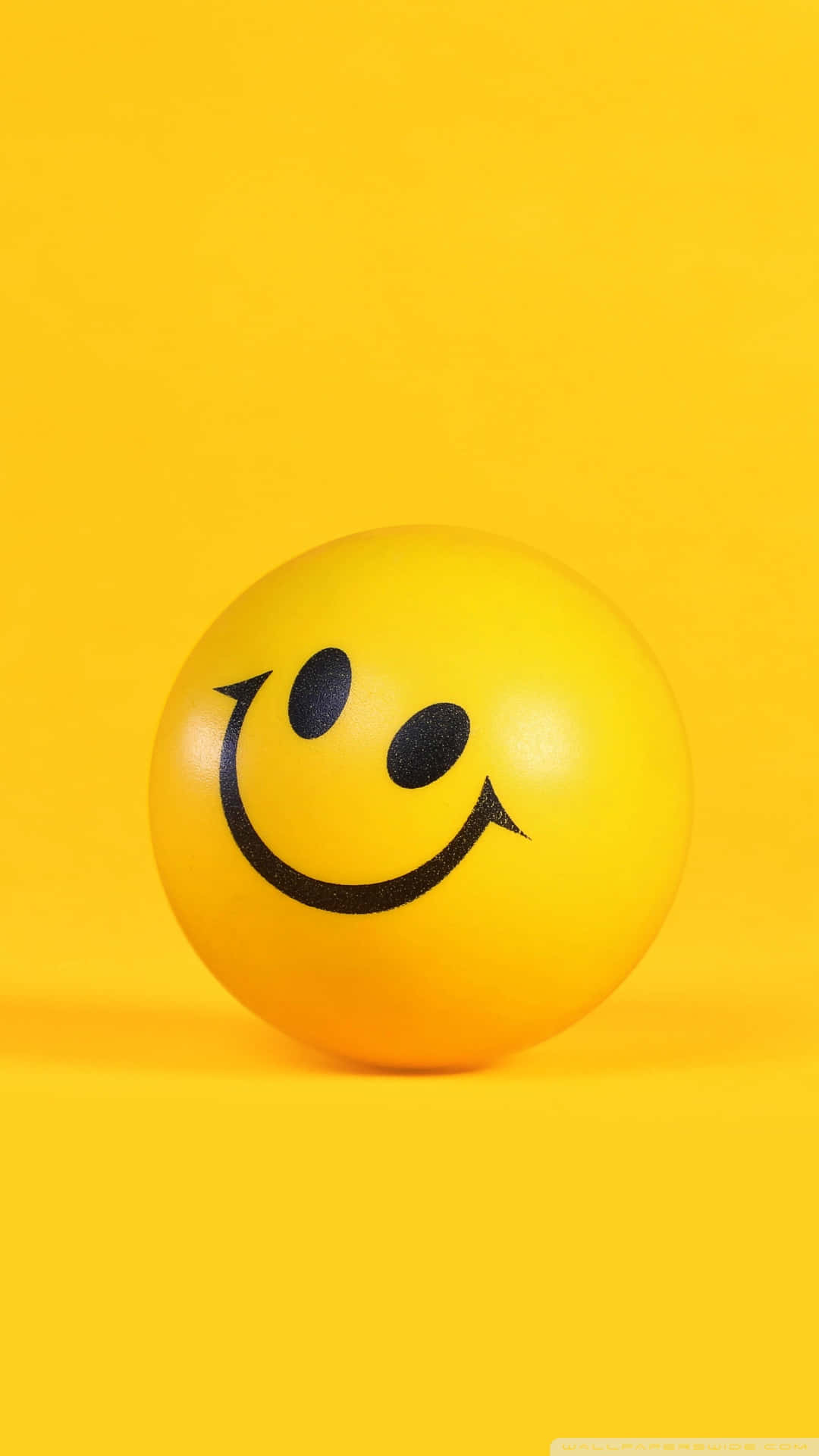 Aesthetic Smiley Face 桌布 壁紙 — 一個明亮的黃色笑臉波波放在純黃色背景上，投射出柔和的陰影。