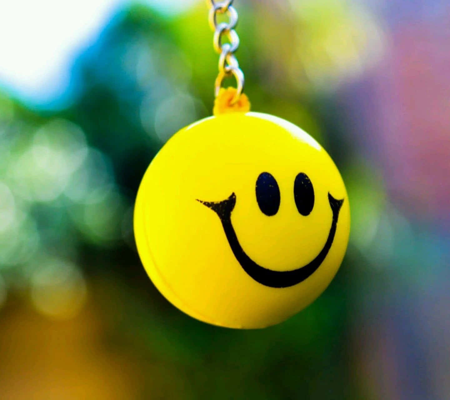 Smile 桌布 壁紙 — 一個明亮的黃色笑臉鑰匙圈掛在色彩繽紛的模糊背景上。