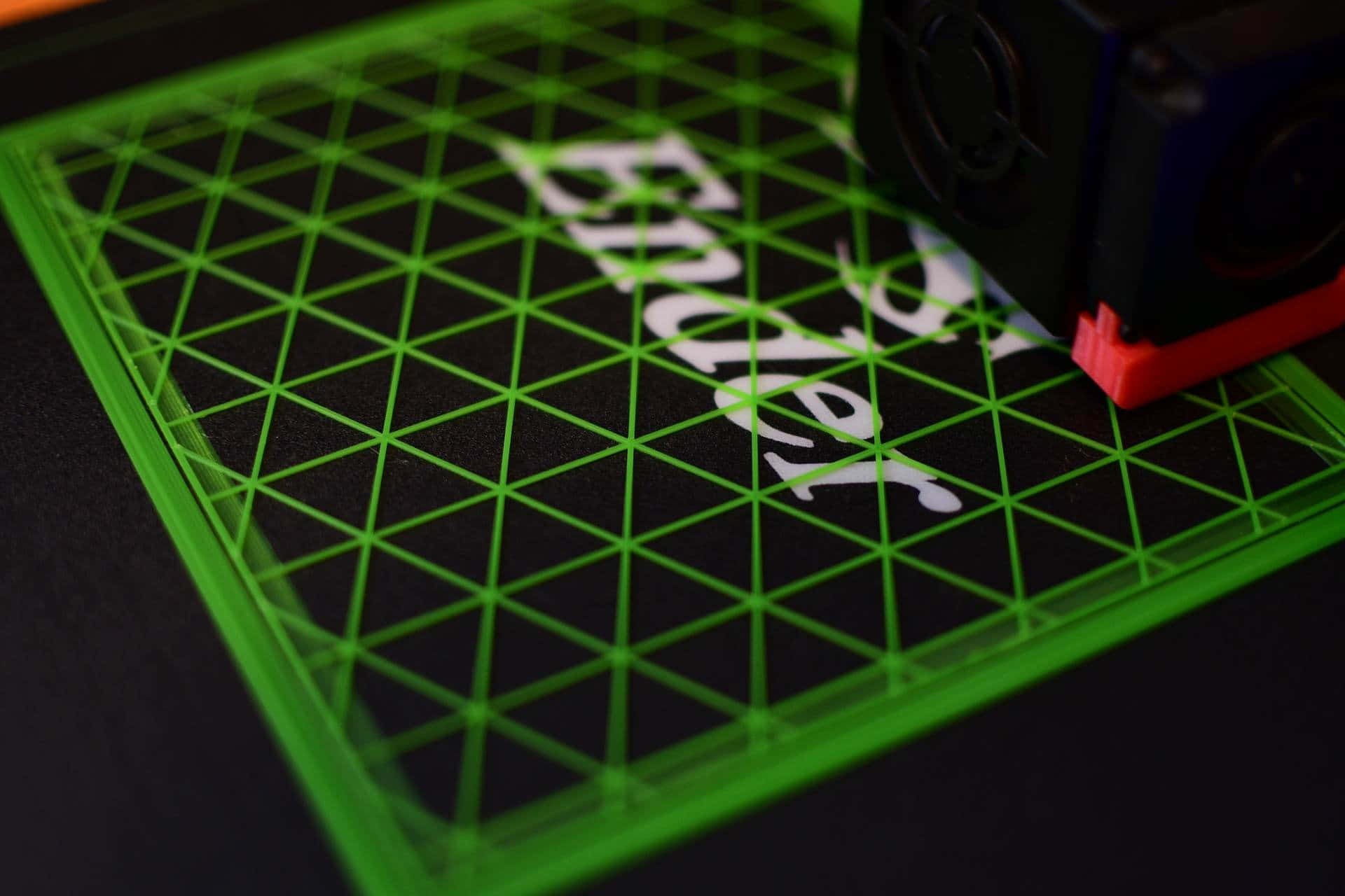 3d Printer 桌布 壁紙 — 一個明亮綠色3D打印機床的近距離特寫，帶有網格線和以白色打印的單詞「Bud」，上面有一個黑色和紅色的打印頭。
