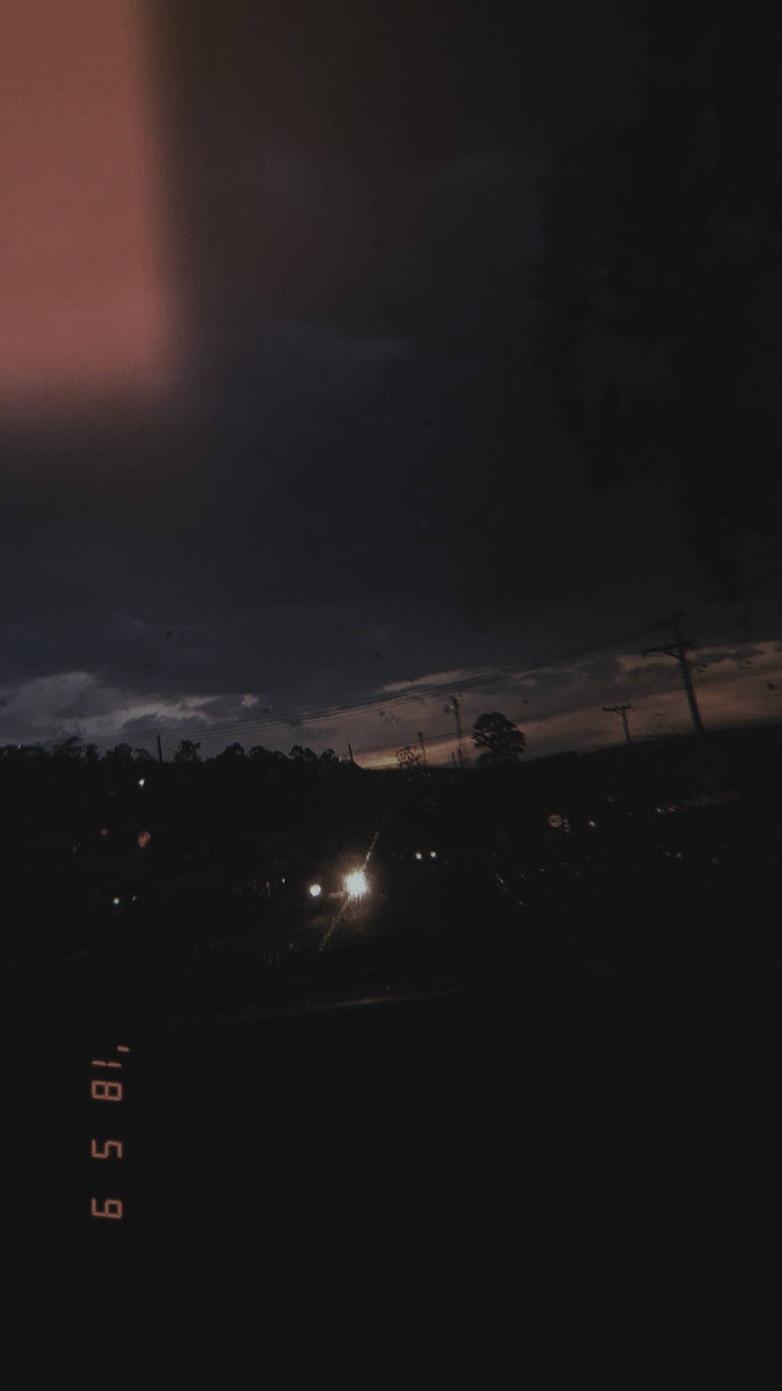  壁紙 — 一個昏暗的城市黃昏場景，遠處的路燈在陰雲密佈的天空和剪影樹木的映襯下閃耀。