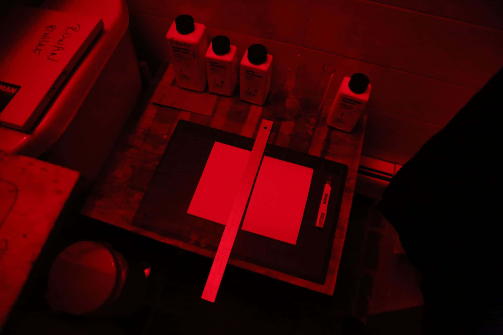 Dark Room 桌布 壁紙 — 一個昏暗的工作空間，沐浴在紅光中，木質表面上放著瓶子和紙張。
