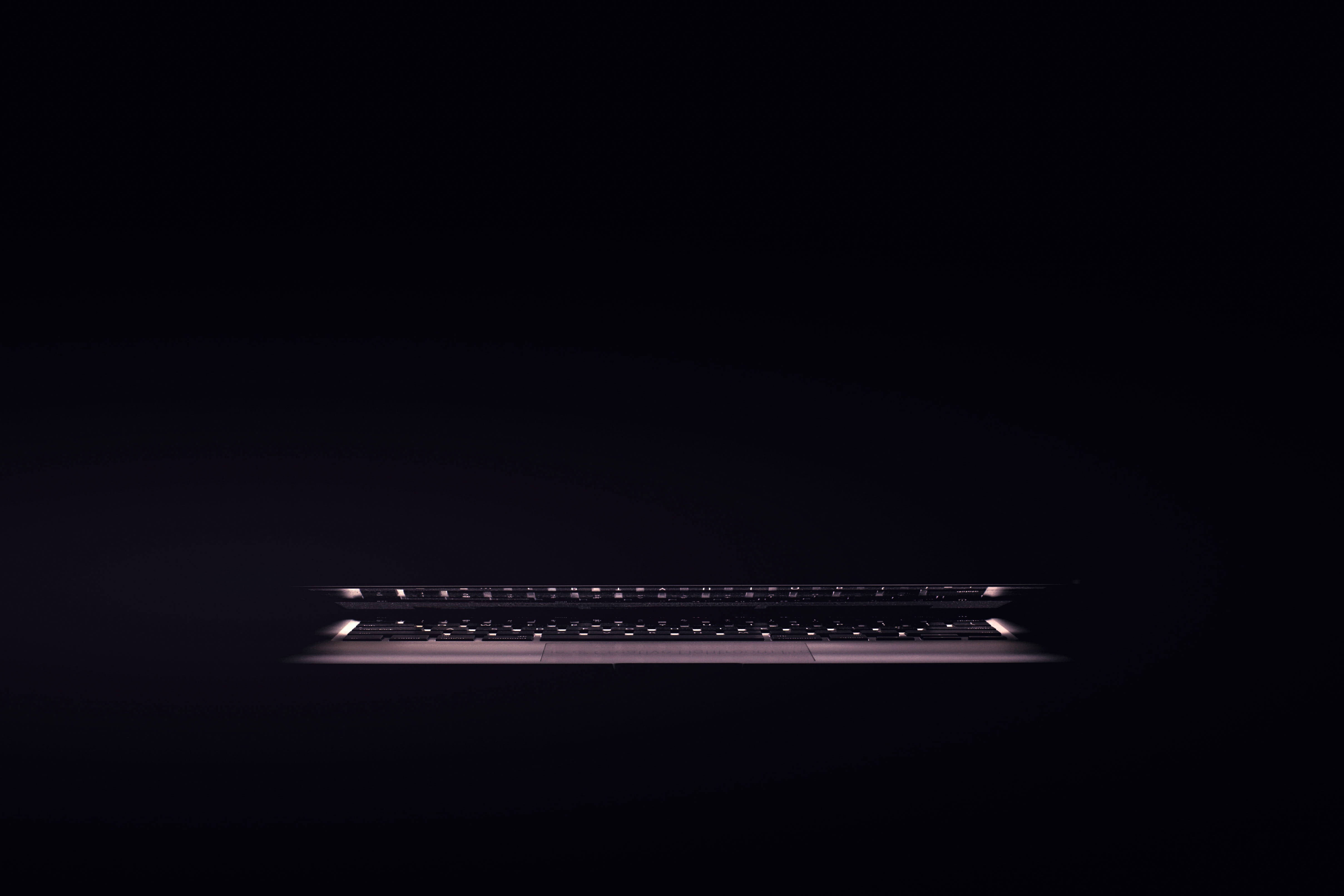 Laptop 桌布 壁紙 — 一個時尚的筆記型電腦鍵盤在漆黑的背景上柔和地發光，投射出微妙的環境光。