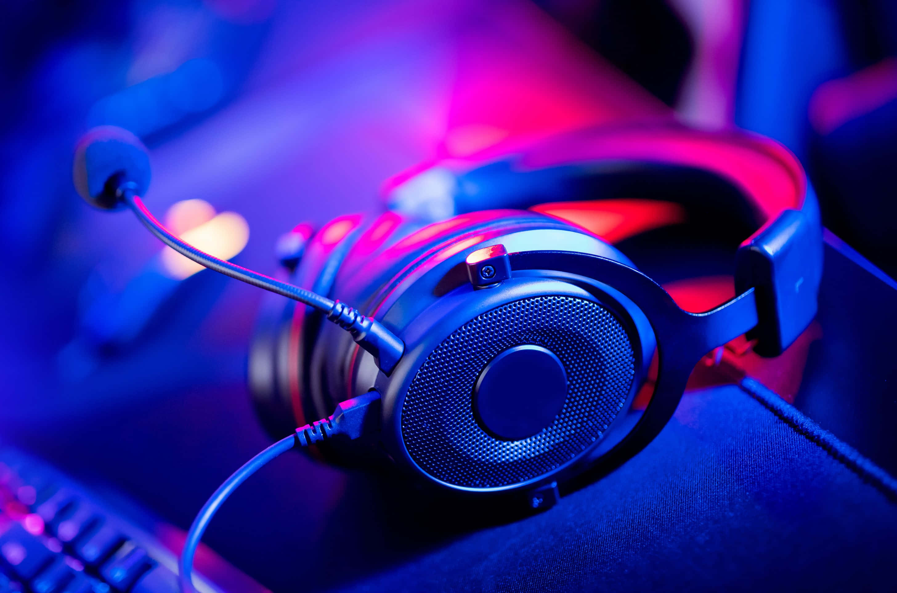 Gaming Headsets 桌布 壁紙 — 一個時尚的遊戲耳機連咪高峰放在鍵盤上，在鮮豔的藍色和粉紅色霓虹燈光下。