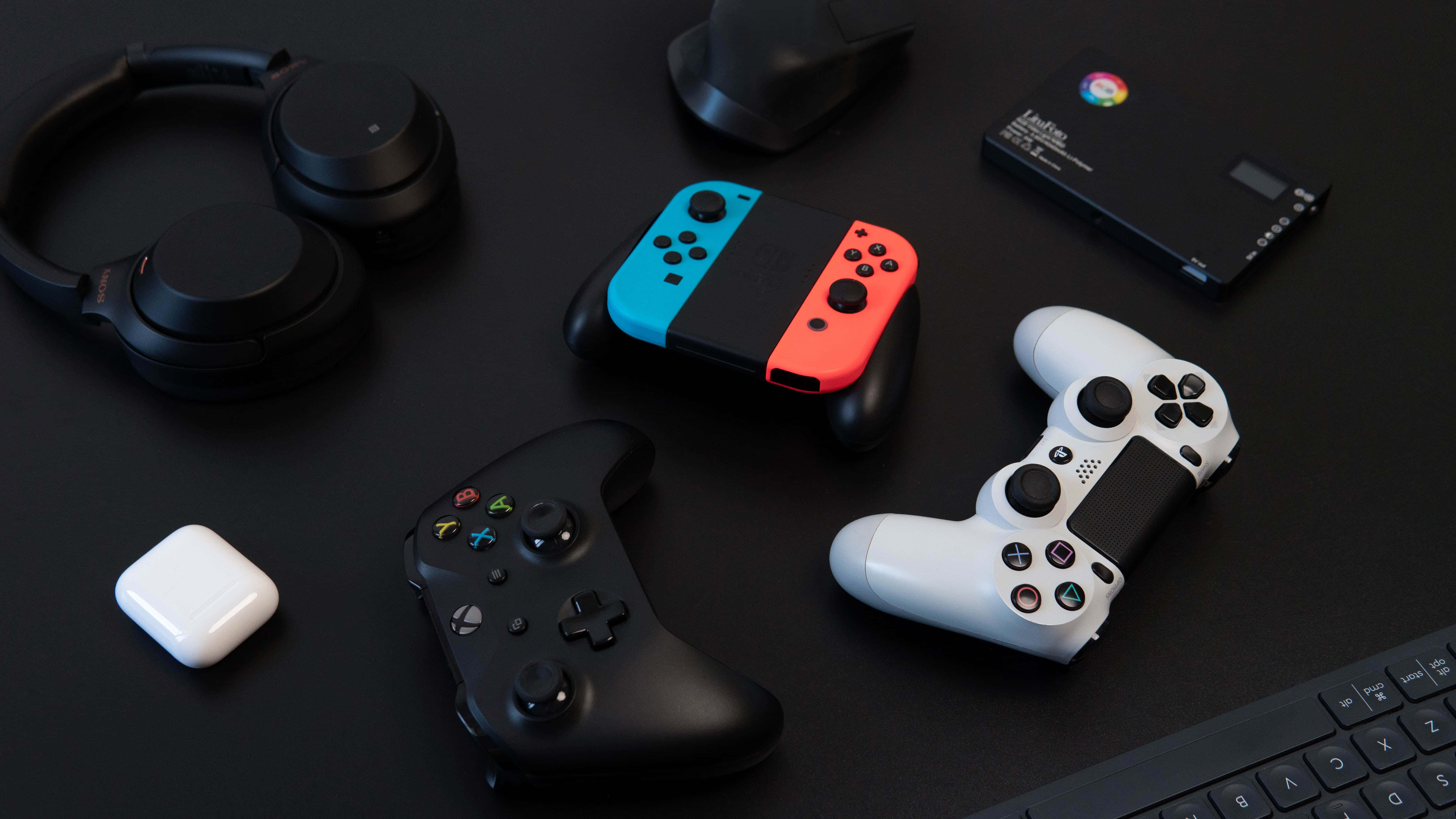 Gaming Consoles 桌布 壁紙 — 一個時尚的遊戲裝備佈置，包括控制器、耳機和鍵盤，放置在磨砂黑色表面上。
