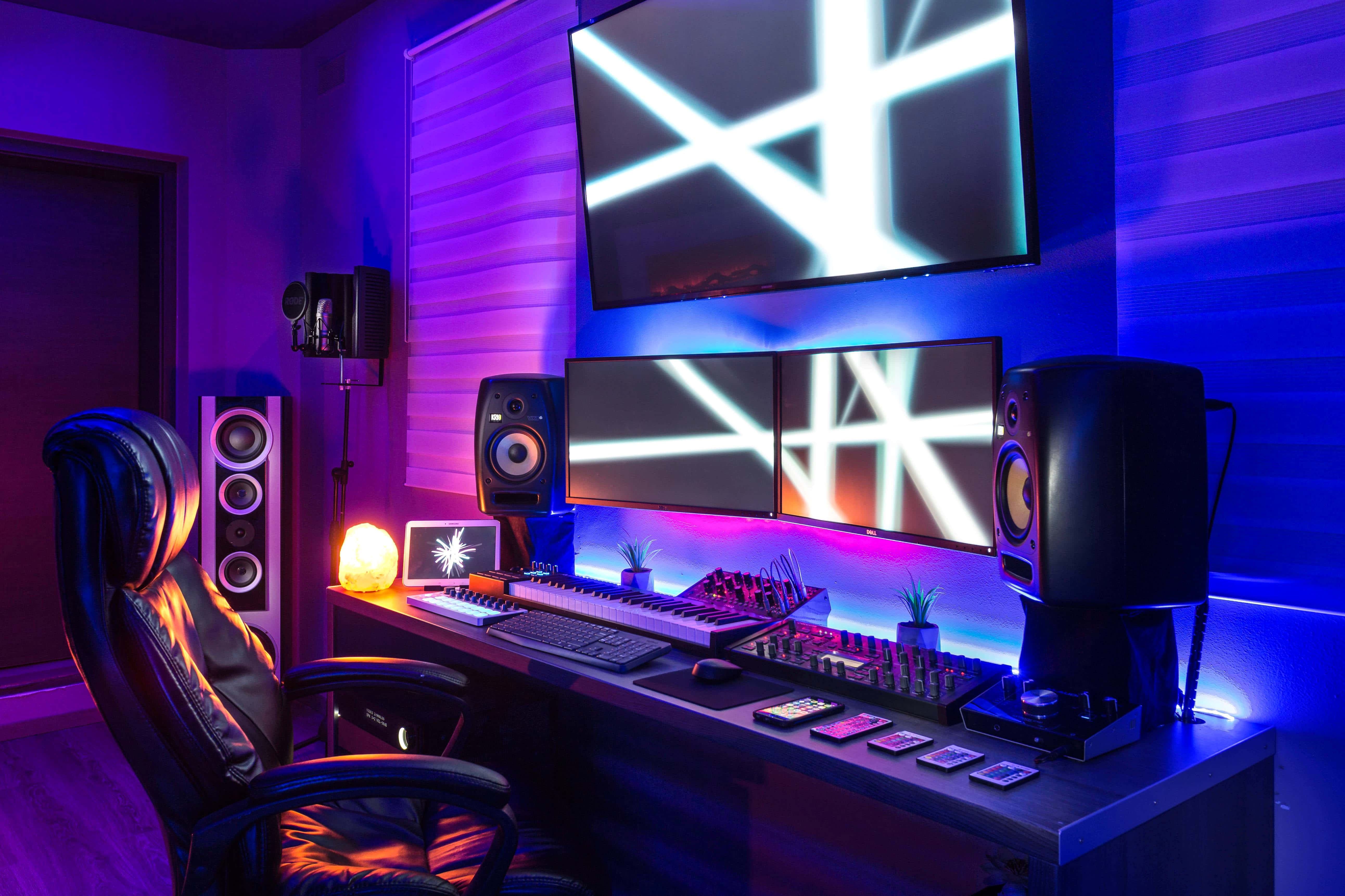 Gaming Pc Setup 桌布 壁紙 — 一個時尚的遊戲設置，沐浴在充滿活力的紫色和藍色霓虹燈光中，配備多個顯示器和高級音響設備。