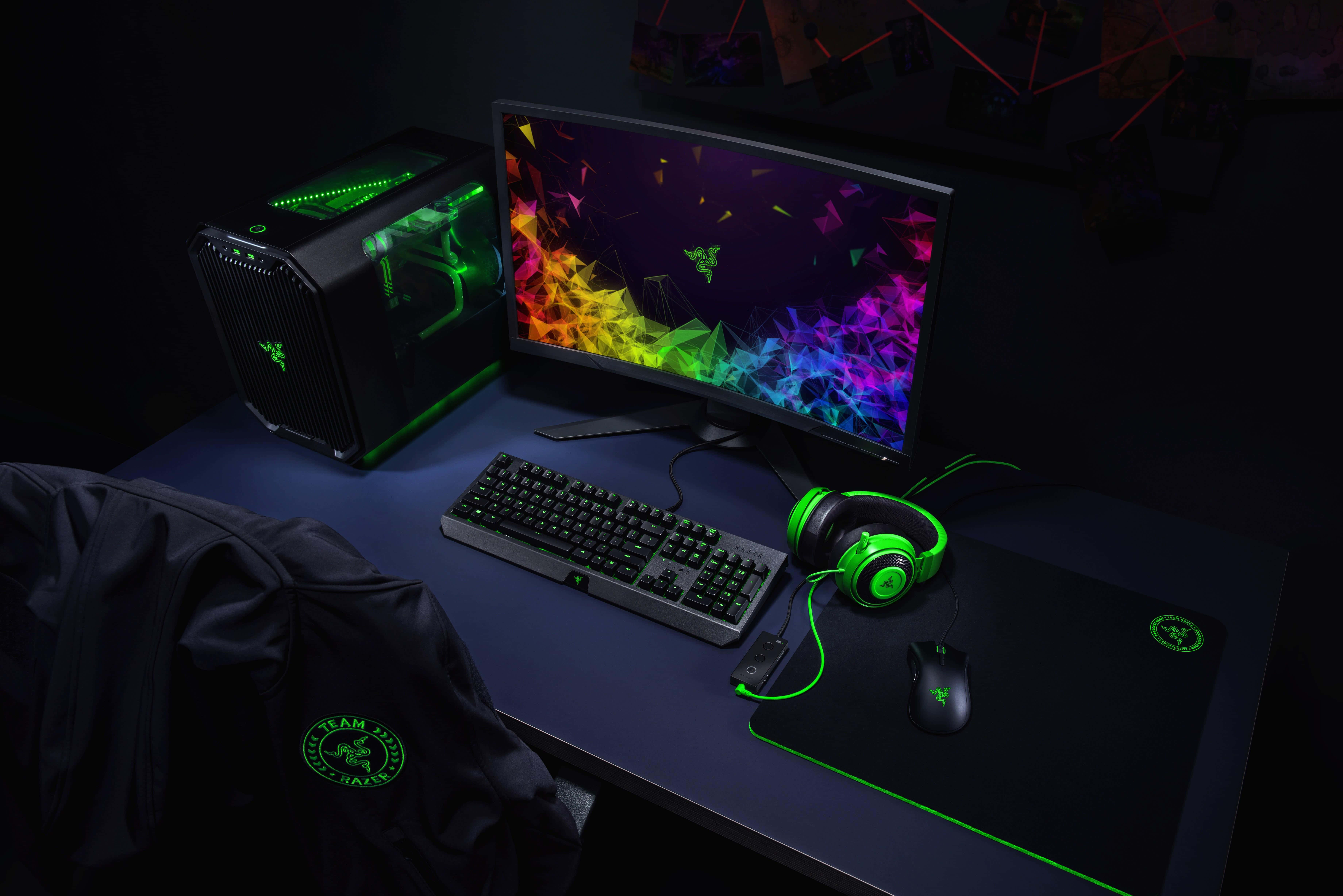 4K Streaming 桌布 壁紙 — 一個時尚的遊戲設置，配備發光的綠色Razer周邊設備和彎曲顯示器上充滿活力的彩虹壁紙，在黑暗的房間中。