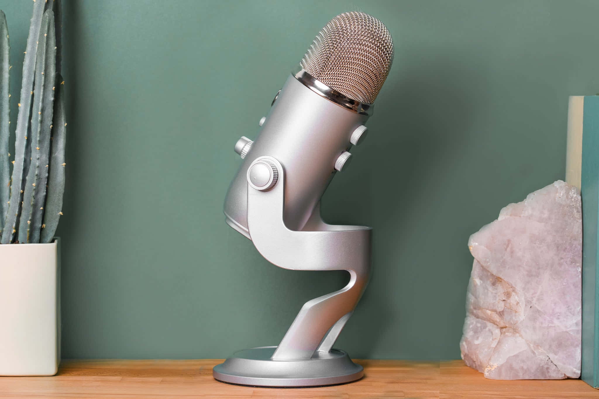 Microphone 桌布 壁紙 — 一個時尚的銀色麥克風放在木桌上，旁邊有仙人掌和粉紅色水晶，背景是柔和的綠色牆壁。