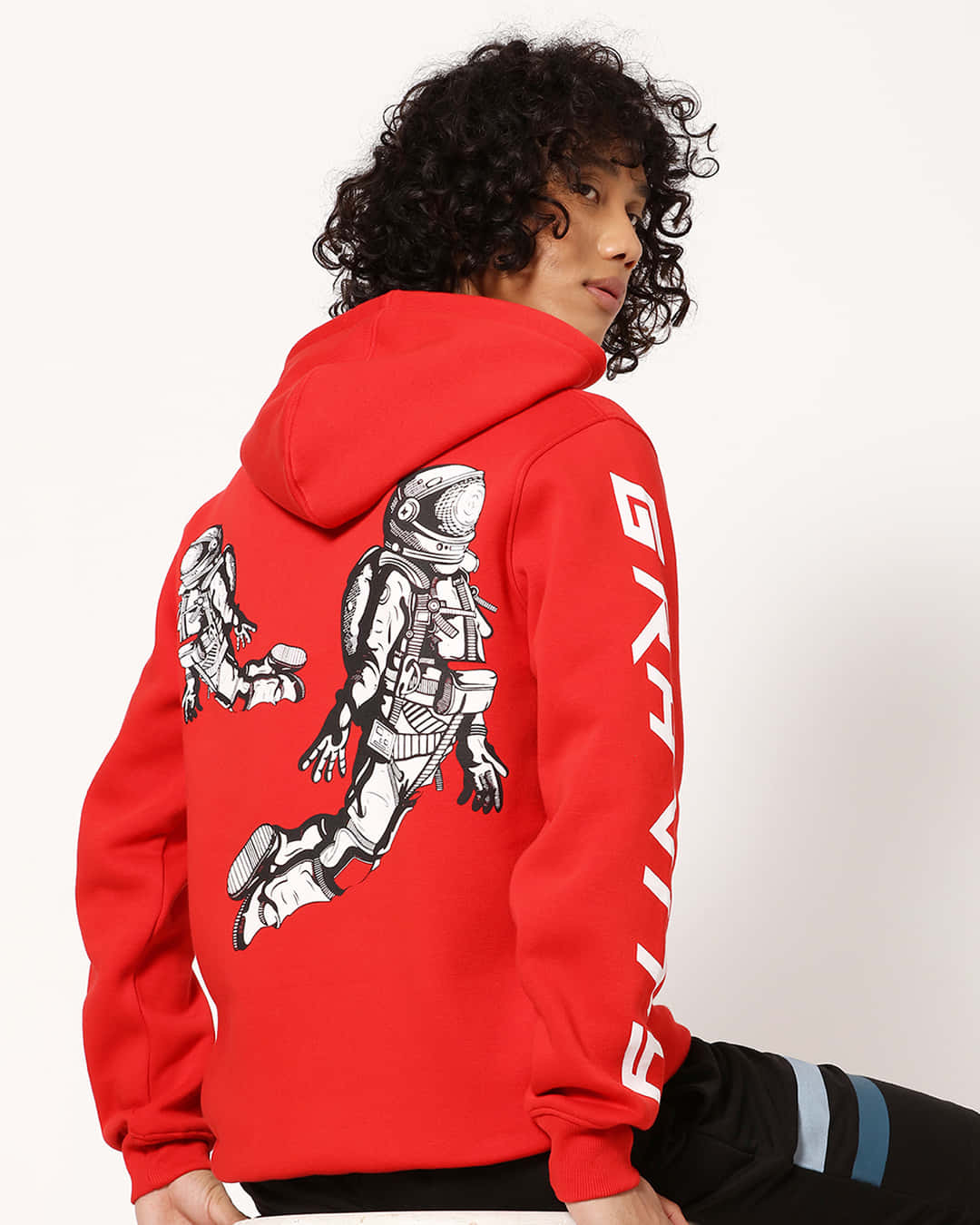 Red Hoodie 桌布 壁紙 — 一個有曲髮嘅人著住一件大膽嘅紅色連帽衫，上面有太空人圖案同袖子上嘅垂直字樣。