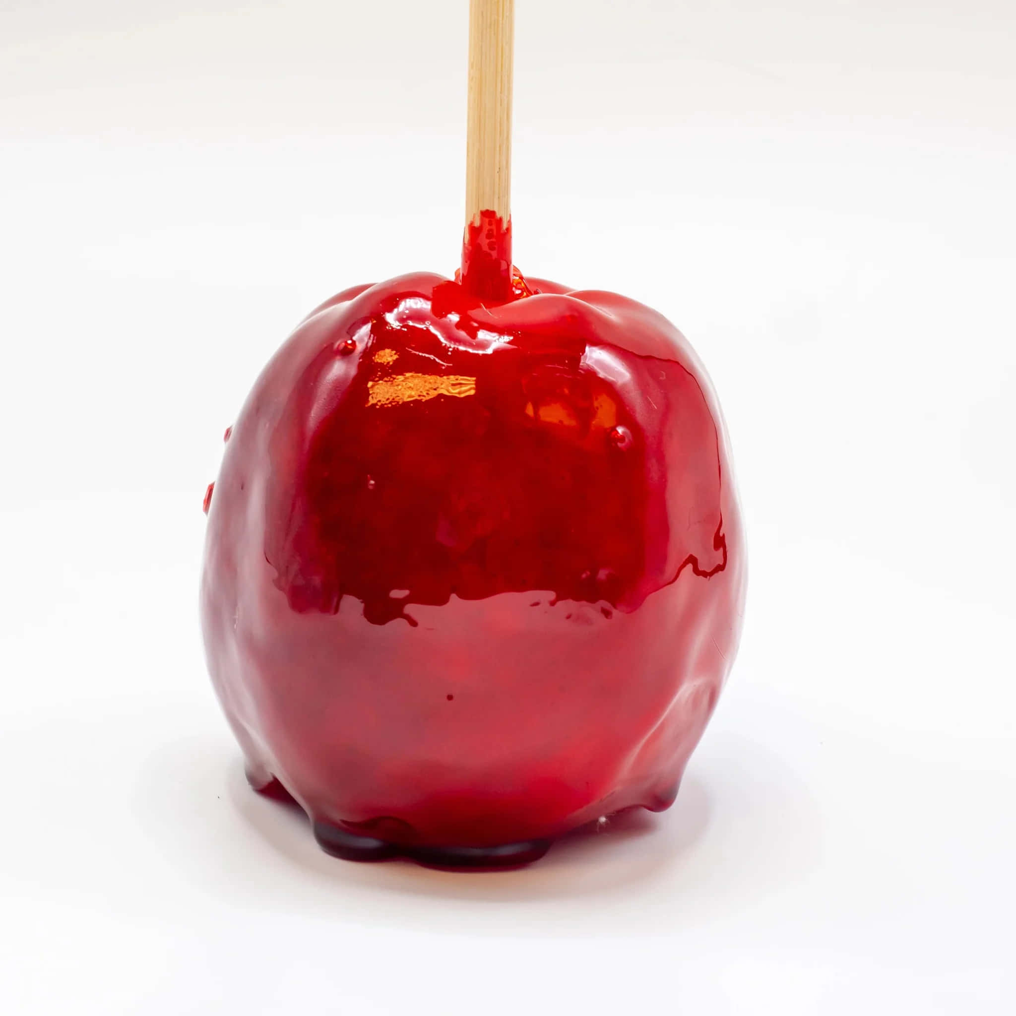 Candy Apples 桌布 壁紙 — 一個有木棍的亮紅色糖蘋果，站在乾淨的白色背景前。