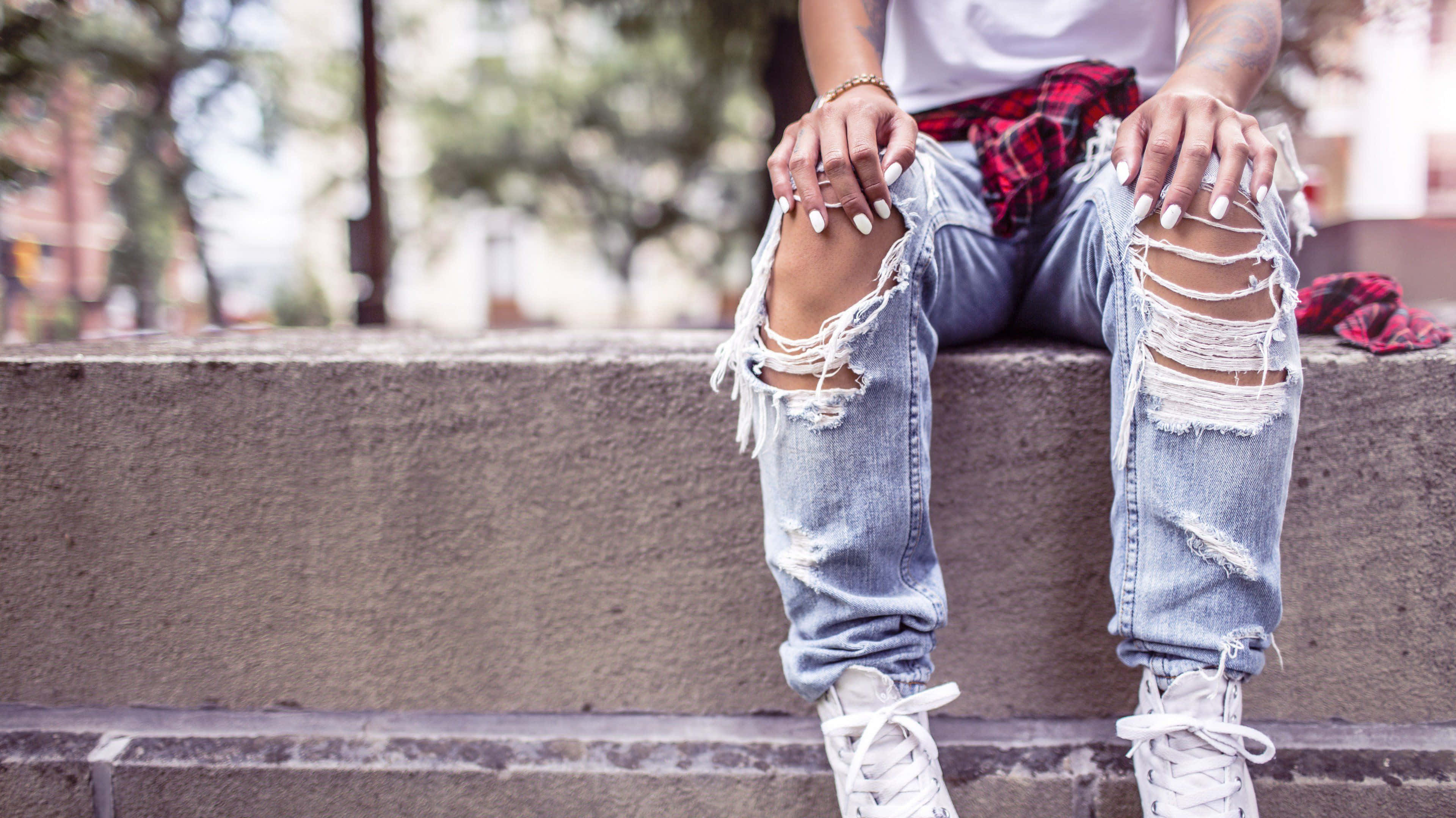 Jeans 桌布 壁紙 — 一個有白色指甲嘅人坐喺石屎梯級上，著住爛牛仔褲同白色波鞋，腰間綁住一件紅色格仔恤衫。