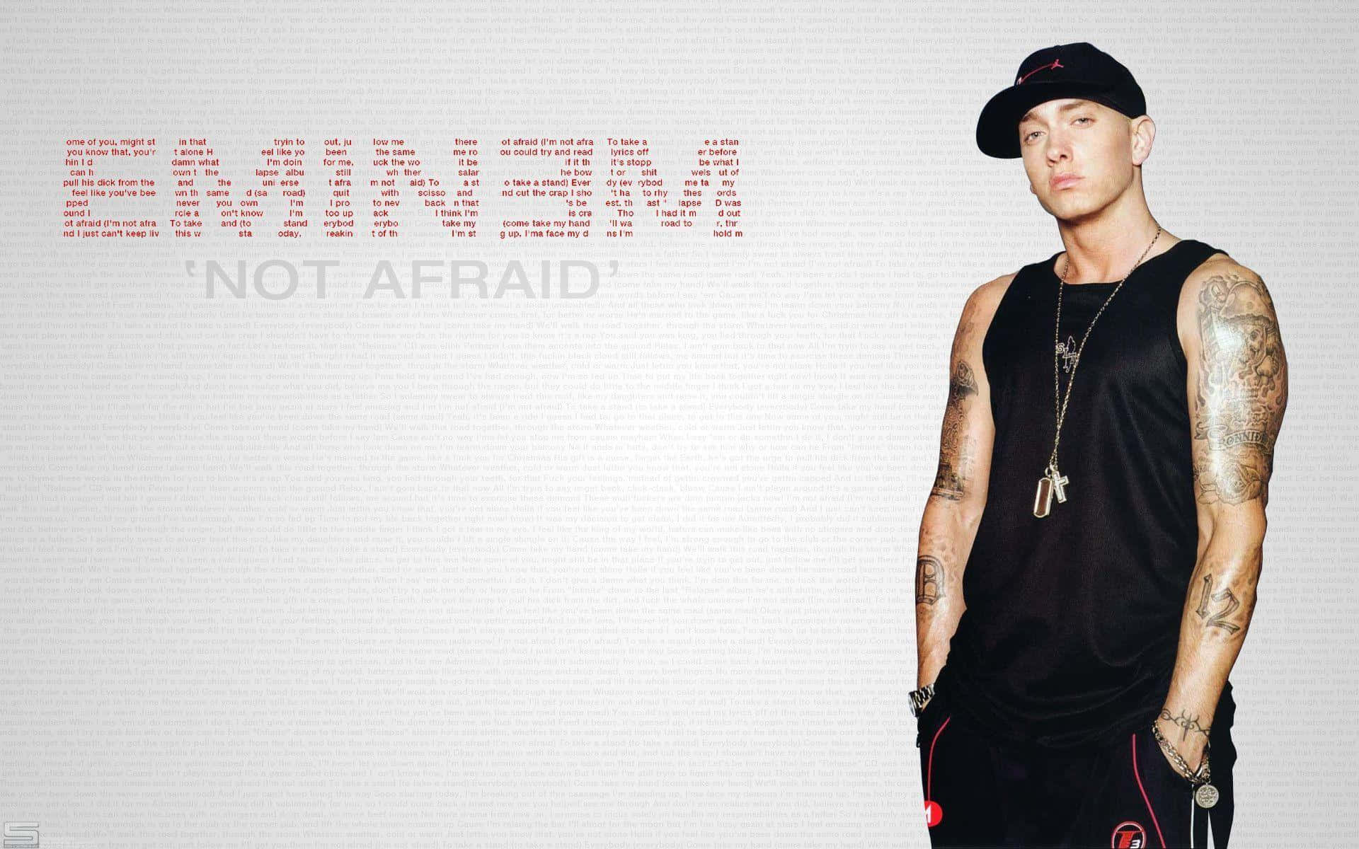 Eminem 桌布 壁紙 — 一個有紋身和戴帽的男人自信地站在他歌曲《Not Afraid》的歌詞旁邊，背景是純色的。