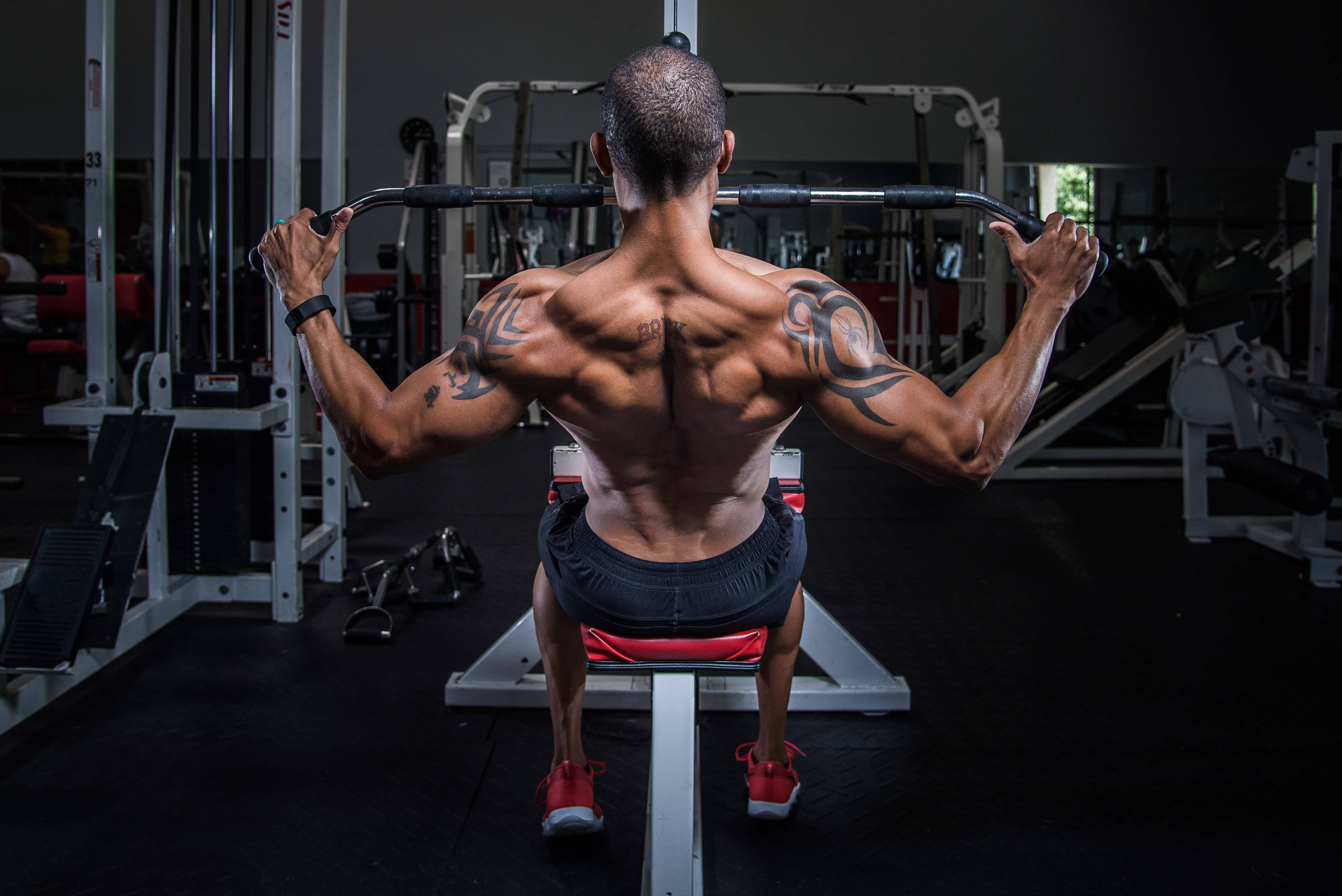 bodybuilders HD 桌布 壁紙 — 一個有紋身的肌肉男在聚焦燈光下用健身器材進行背部訓練。