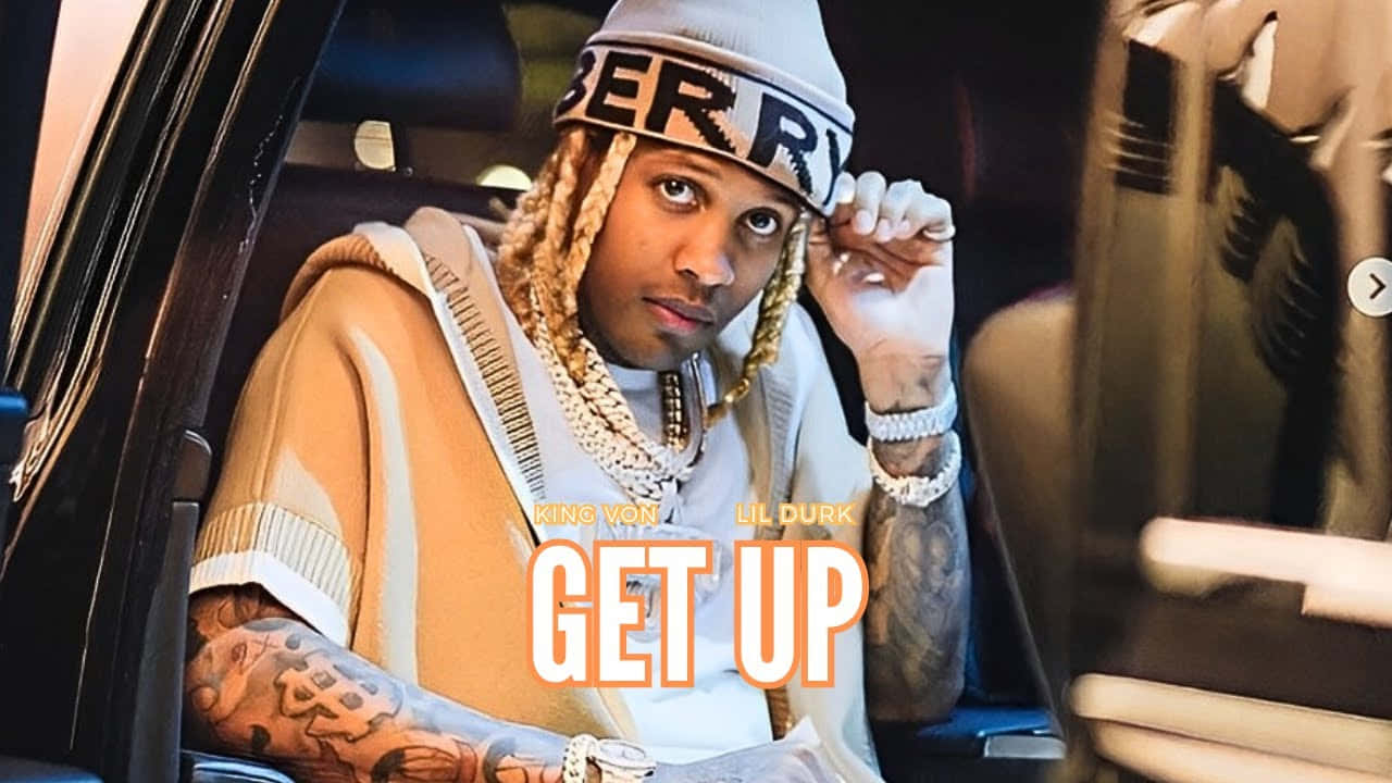 King Von And Lil Durk 桌布 壁紙 — 一個有辮子頭髮和紋身的男人坐在車裡，戴著冷帽和鏈條，直視鏡頭。