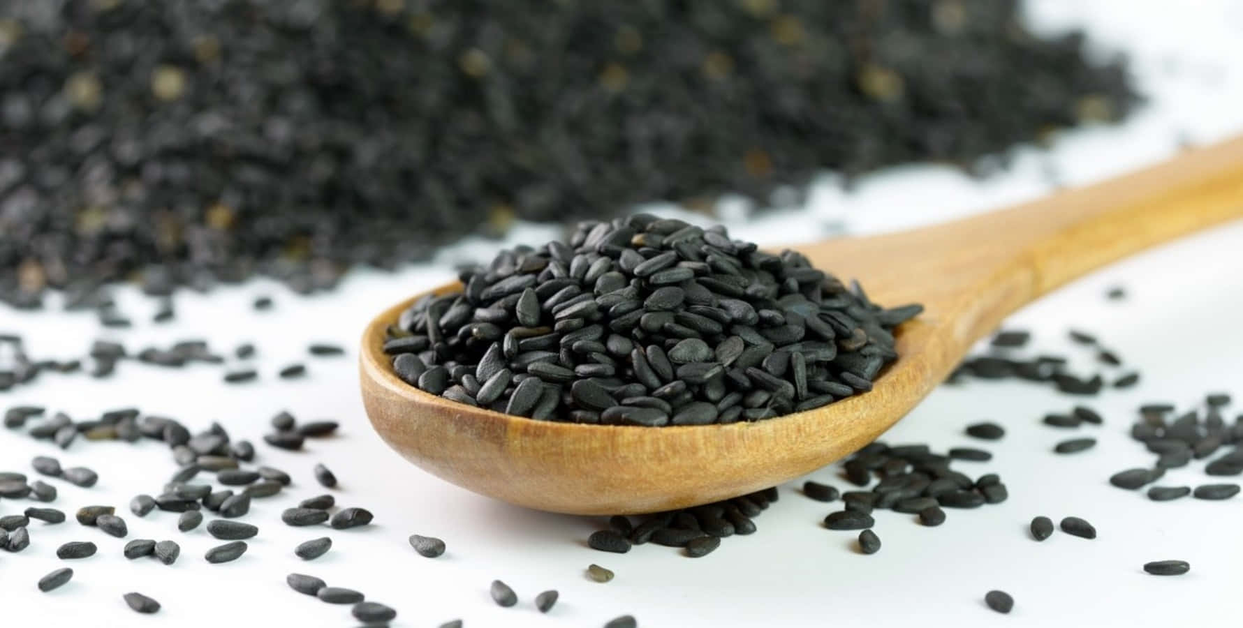 Black Sesame 桌布 壁紙 — 一個木勺盛滿光澤的黑芝麻，溢出在純白背景上，散落著芝麻。