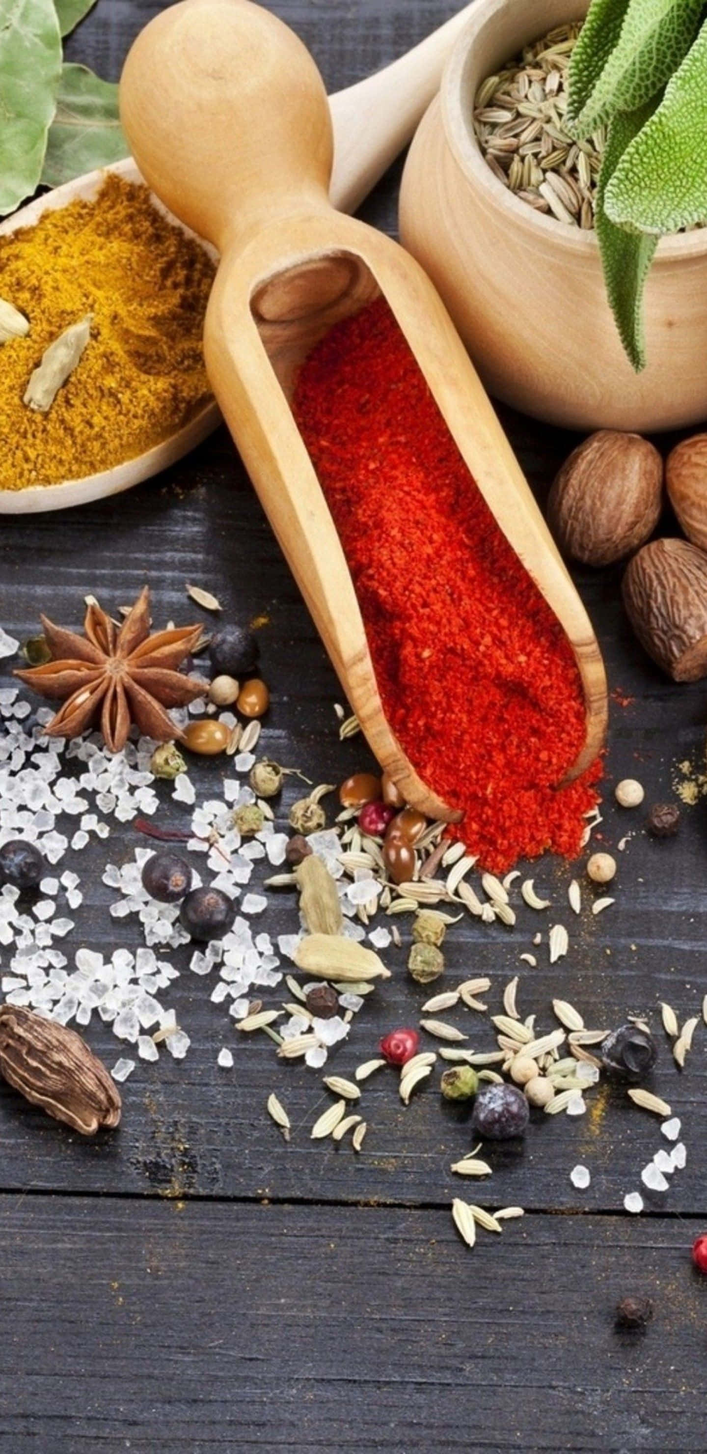 Spice 桌布 壁紙 — 一個木勺盛滿鮮紅辣椒粉，放在深色鄉村風木質表面上，周圍散落著各種香料和香草。
