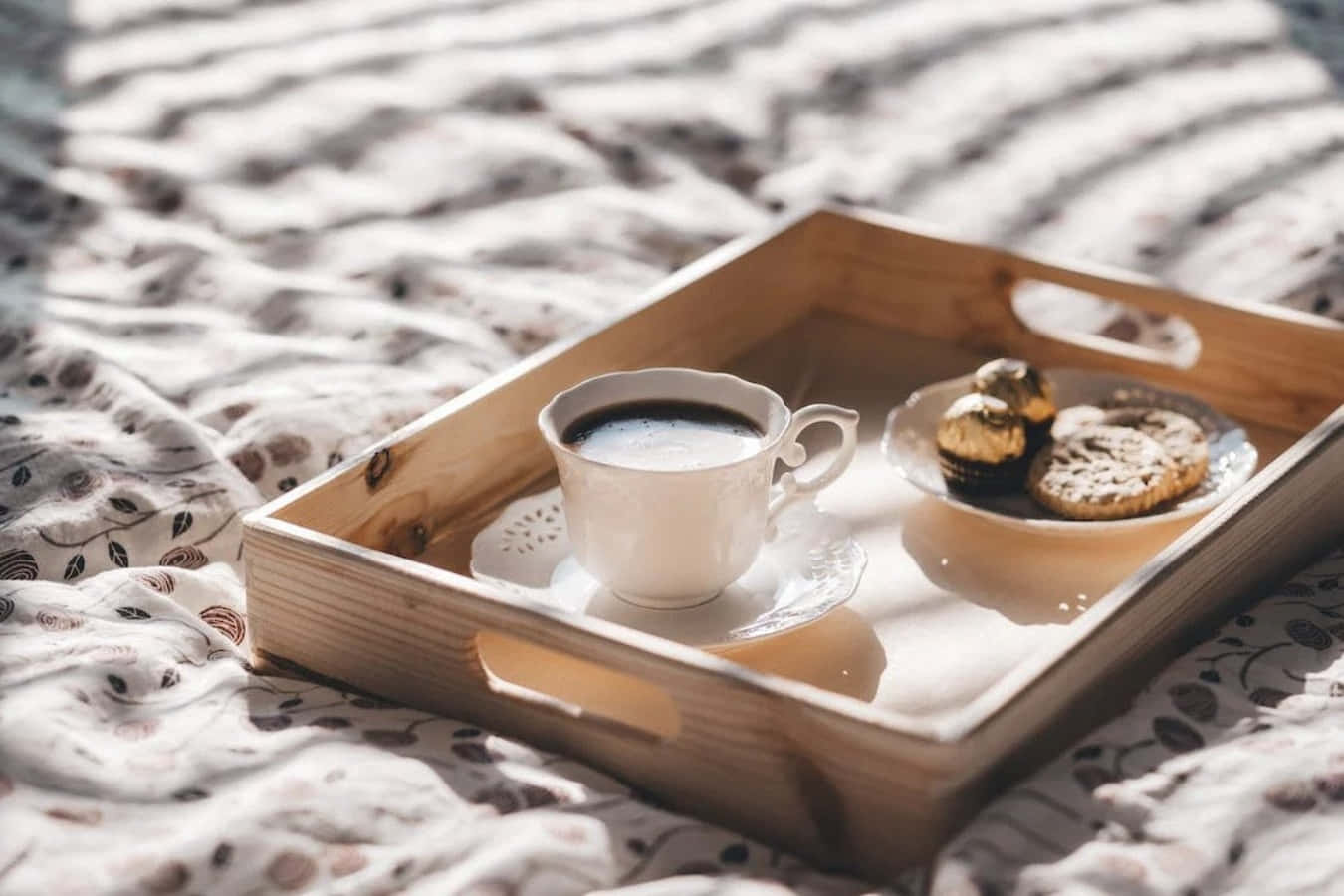 Coffee Cup 桌布 壁紙 — 一個木托盤上放著一個白色咖啡杯和朱古力曲奇，放在圖案床罩上，沐浴在柔和的晨光中。