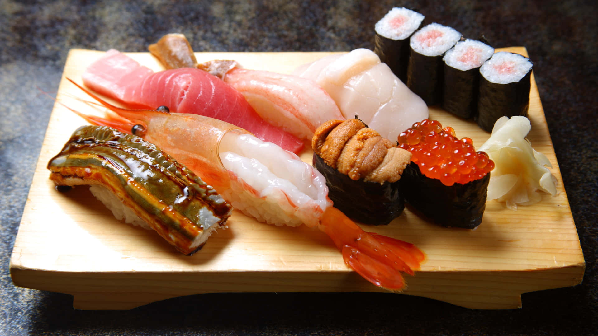 Sushi 桌布 壁紙 — 一個木盤在溫暖燈光下展示各種新鮮壽司，包括吞拿魚、蝦、鰻魚和三文魚籽。