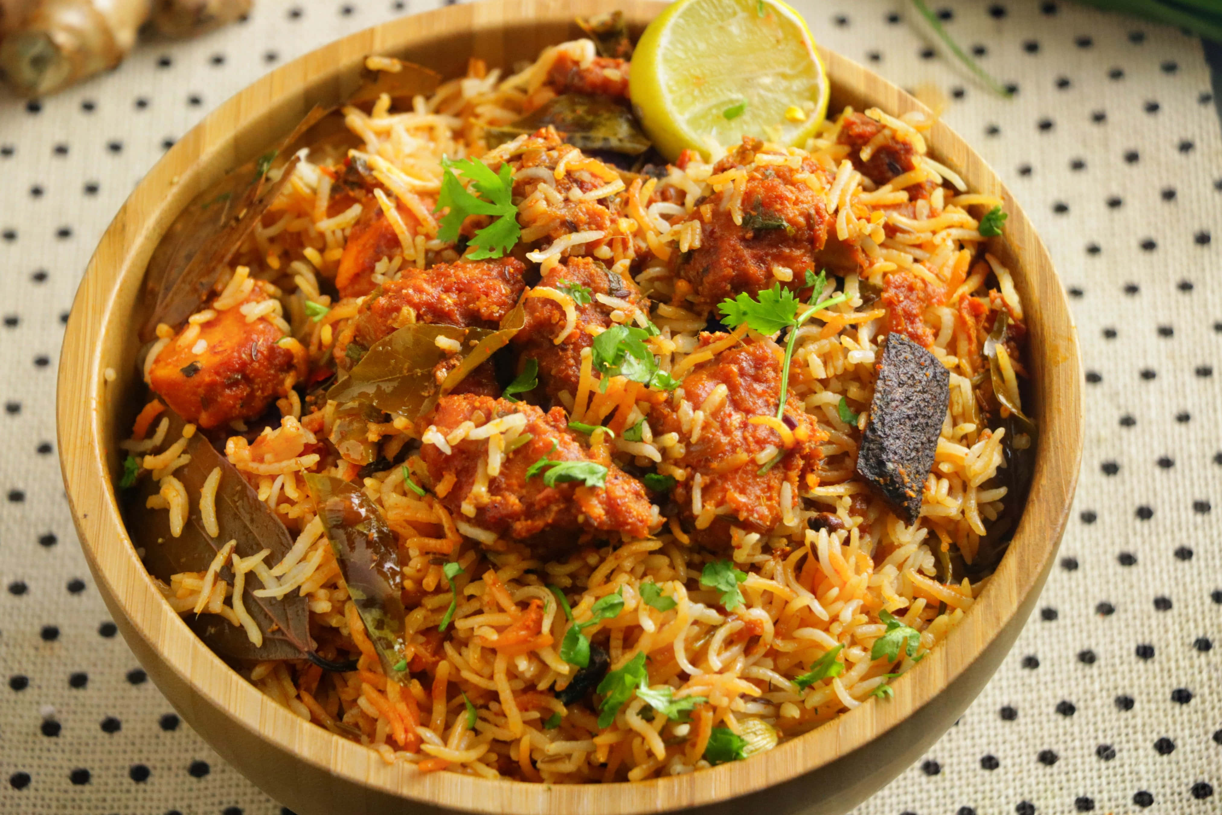Biryani 桌布 壁紙 — 一個木碗盛滿香氣撲鼻的印度香飯和嫩肉塊，上面點綴著新鮮芫荽和青檸角。