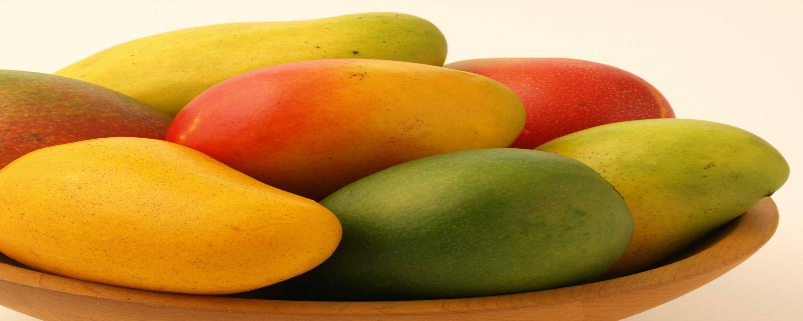 Mango 桌布 壁紙 — 一個木碗盛載著色彩繽紛的成熟芒果，呈現鮮豔的黃色、紅色和綠色色調，背景為純白色。