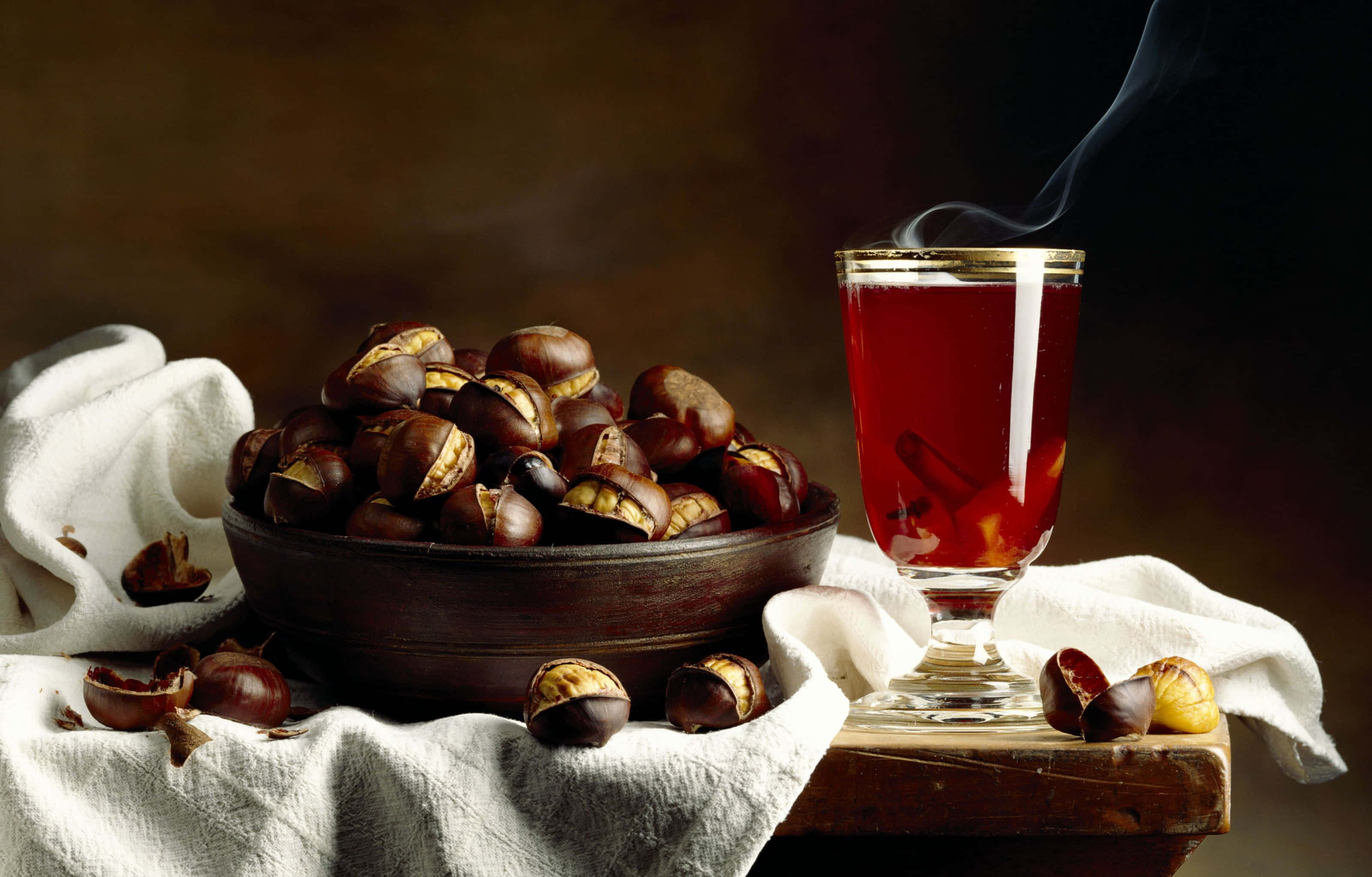Mulled Wine 桌布 壁紙 — 一個木碗裝滿烤栗子，旁邊放著一杯冒著熱氣的濃郁紅色飲料，放在質樸的布上。