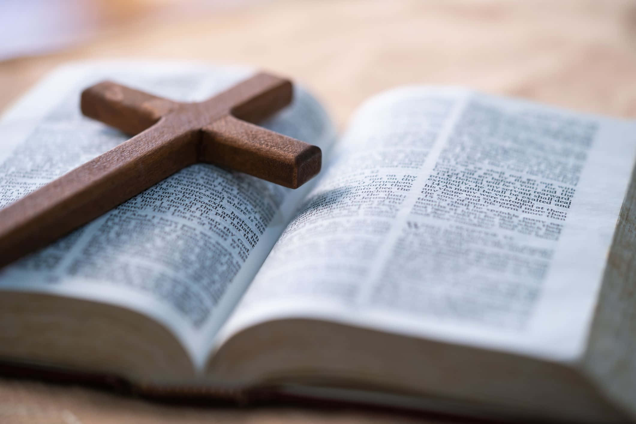 Religious Easter 桌布 壁紙 — 一個木製十字架放在一本打開的聖經上，置於溫暖的木質表面，柔和自然光線照射。