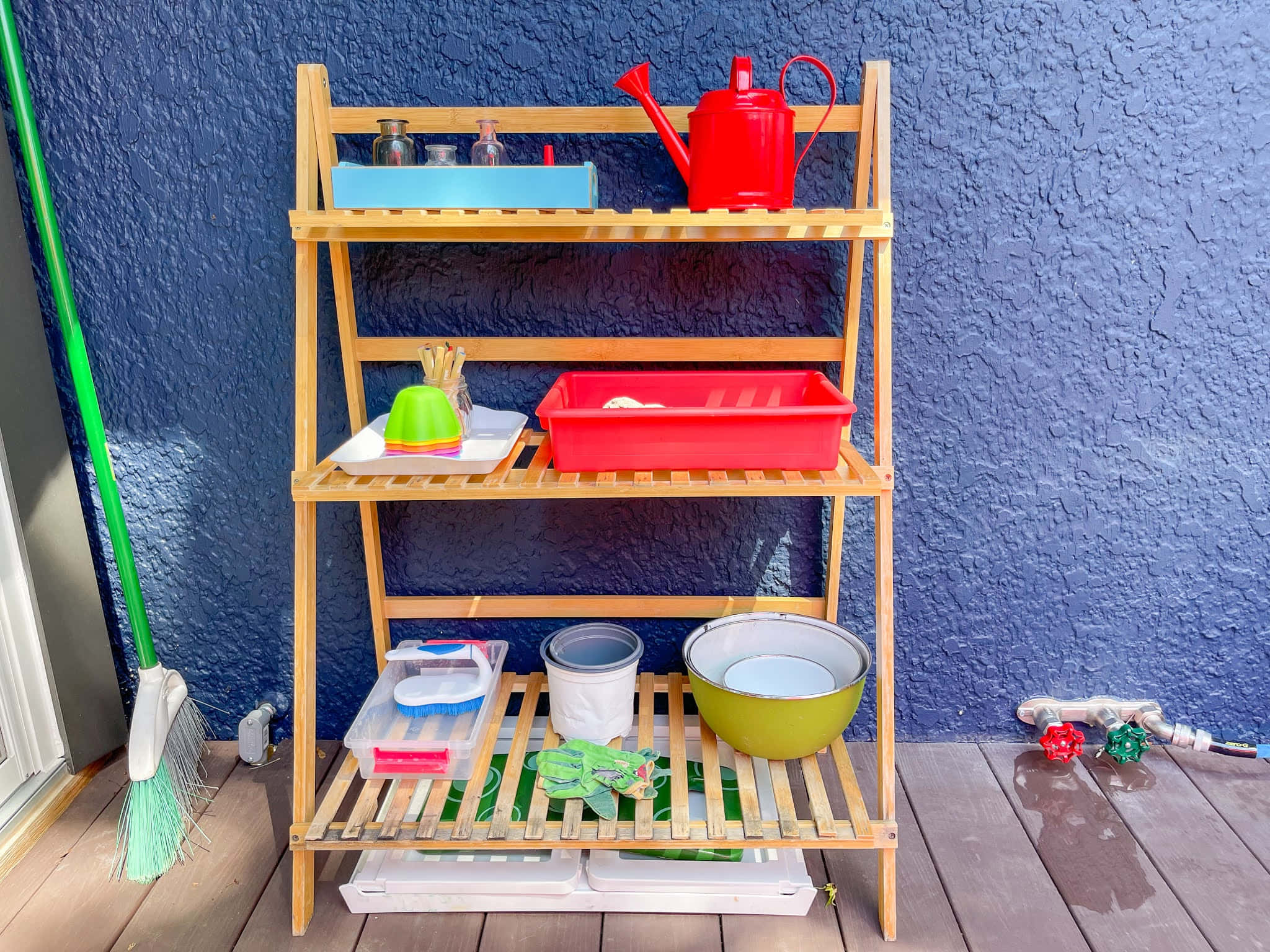 Outdoor Activities 桌布 壁紙 — 一個木製戶外架在木甲板上，靠著紋理藍色牆壁，擺放著色彩繽紛的園藝工具和容器。