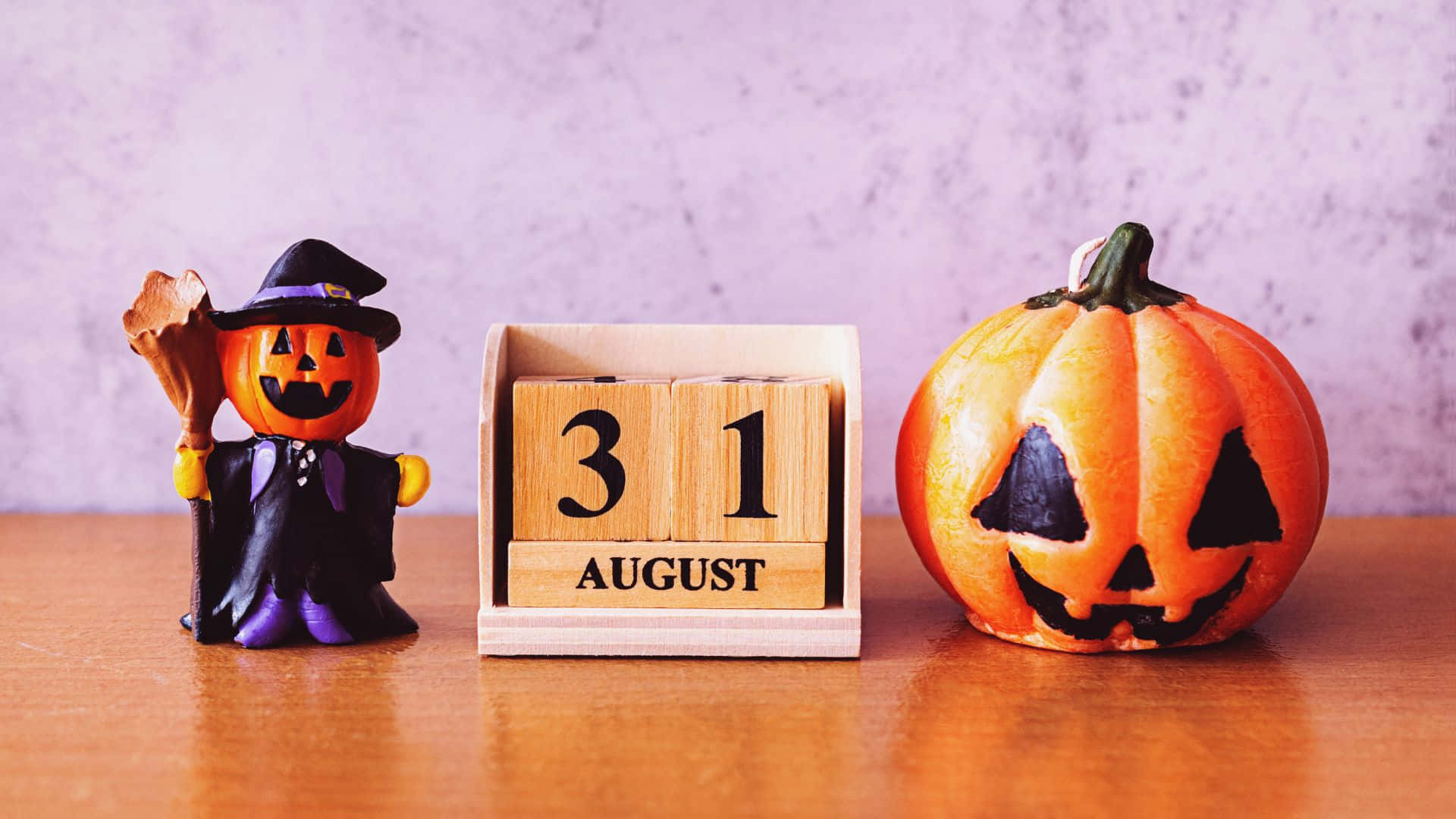 October 31st 桌布 壁紙 — 一個木製日曆顯示8月31日，兩側有一個女巫公仔和一個雕刻的南瓜燈，放在溫暖的木質表面上。
