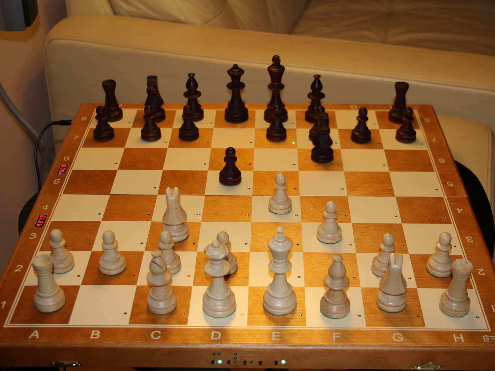 Chessboard 桌布 壁紙 — 一個木製棋盤，上面擺放著深色和淺色的棋子準備對弈，棋盤擱在米色梳化旁邊的桌子上。
