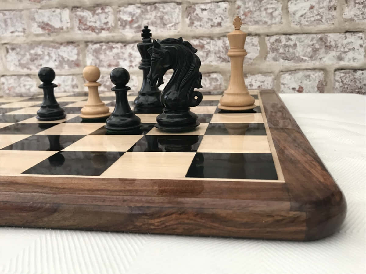 Chessboard 桌布 壁紙 — 一個木製棋盤的特寫，上面有黑色和淺色木製棋子，背景是風化的磚牆。