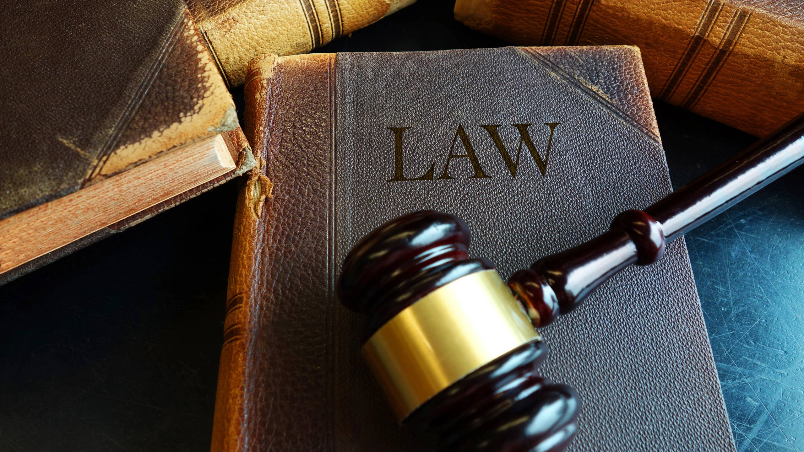 Lawyer 桌布 壁紙 — 一個木製法槌的特寫，帶有金色環帶，放在一本名為「法律」的皮革裝訂法律書上，周圍是陳舊的法律典籍。